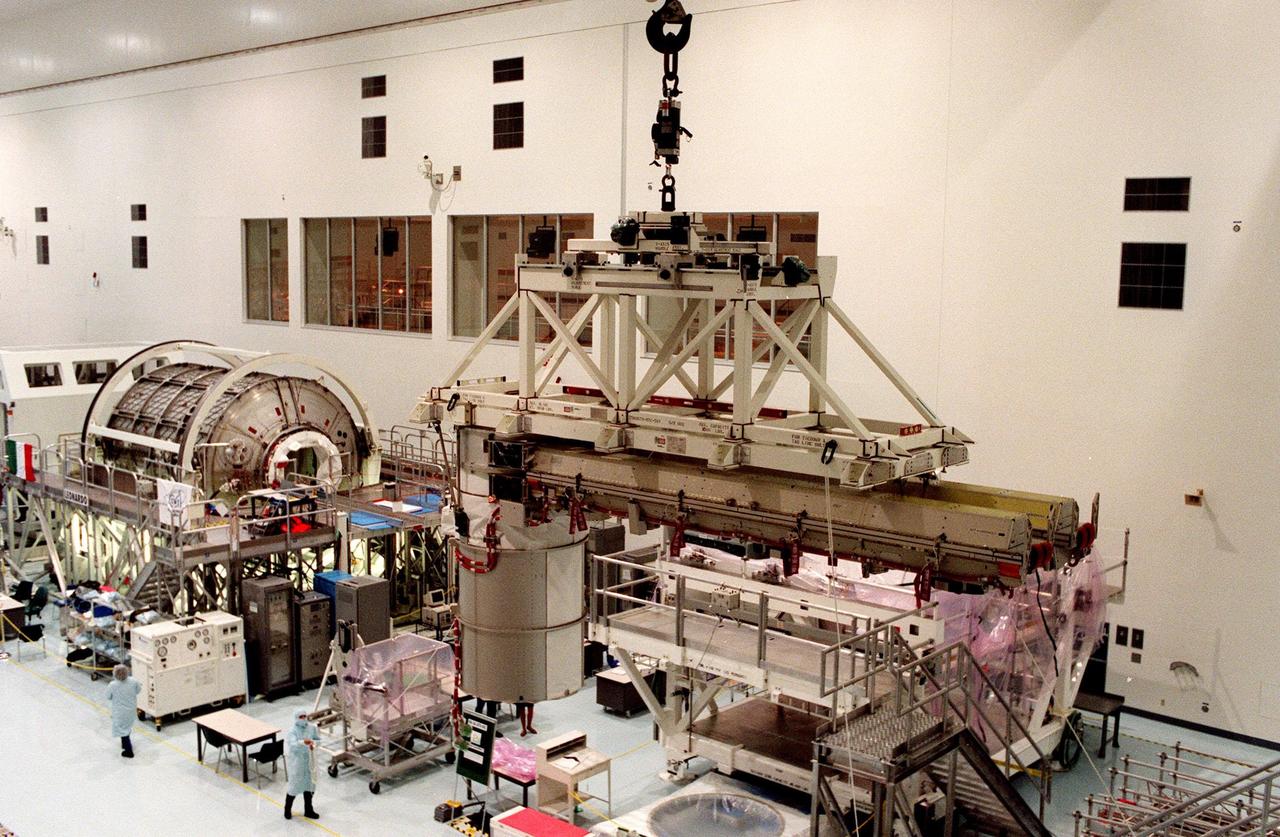 In the Space Station Processing Facility, the overhead crane slowly moves solar panels intended for the International Space Station (ISS). The panels are the first set of U.S.-provided solar arrays and batteries for ISS, scheduled to be part of mission STS-97 in December 1999. The mission, fifth in the U.S. flights for construction of ISS, will build and enhance the capabilities of the Space Station. It will deliver the solar panels as well as radiators to provide cooling. The Shuttle will spend 5 days docked to the station, which at that time will be staffed by the first station crew. Two space walks will be conducted to complete assembly operations while the arrays are attached and unfurled. A communications system for voice and telemetry also will be installed. At the left of the crane and panels is the Multipurpose Logistics Module (MPLM), the Leonardo A reusable logistics carrier, the MPLM is scheduled to be launched on Space Shuttle Mission STS-100, targeted for April 2000