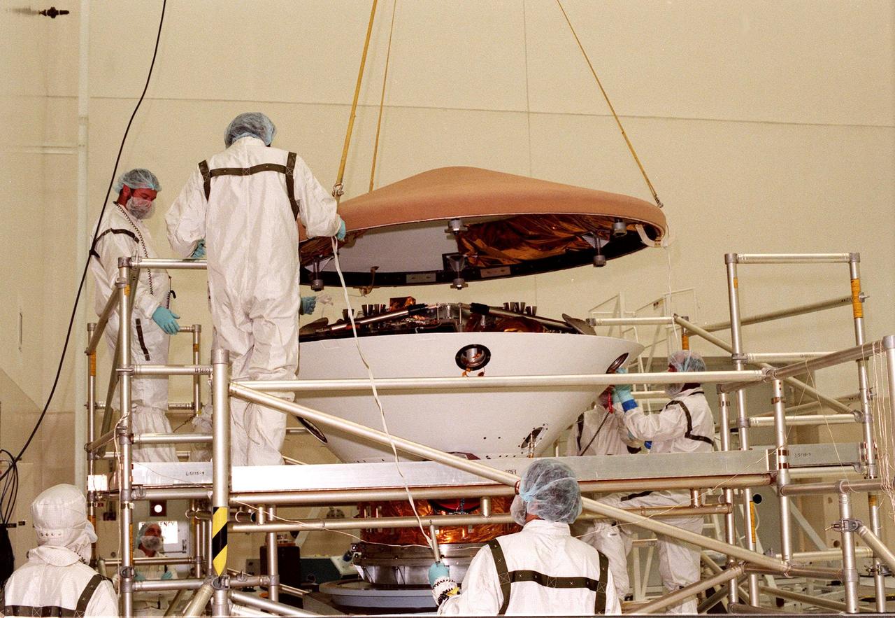 In the Spacecraft Assembly and Encapsulation Facility-2 (SAEF-2), workers lower the heat shield onto the Mars Polar Lander. Scheduled to be launched on Jan. 3, 1999, the lander is a solar-powered spacecraft designed to touch down on the Martian surface near the northern-most boundary of the south pole in order to study the water cycle there. The lander also will help scientists learn more about climate change and current resources on Mars, studying such things as frost, dust, water vapor and condensates in the Martian atmosphere. It is the second spacecraft to be launched in a pair of Mars '98 missions. The first is the Mars Climate Orbiter, which is due to be launched aboard a Delta II rocket from Launch Complex 17A on Dec. 11, 1998