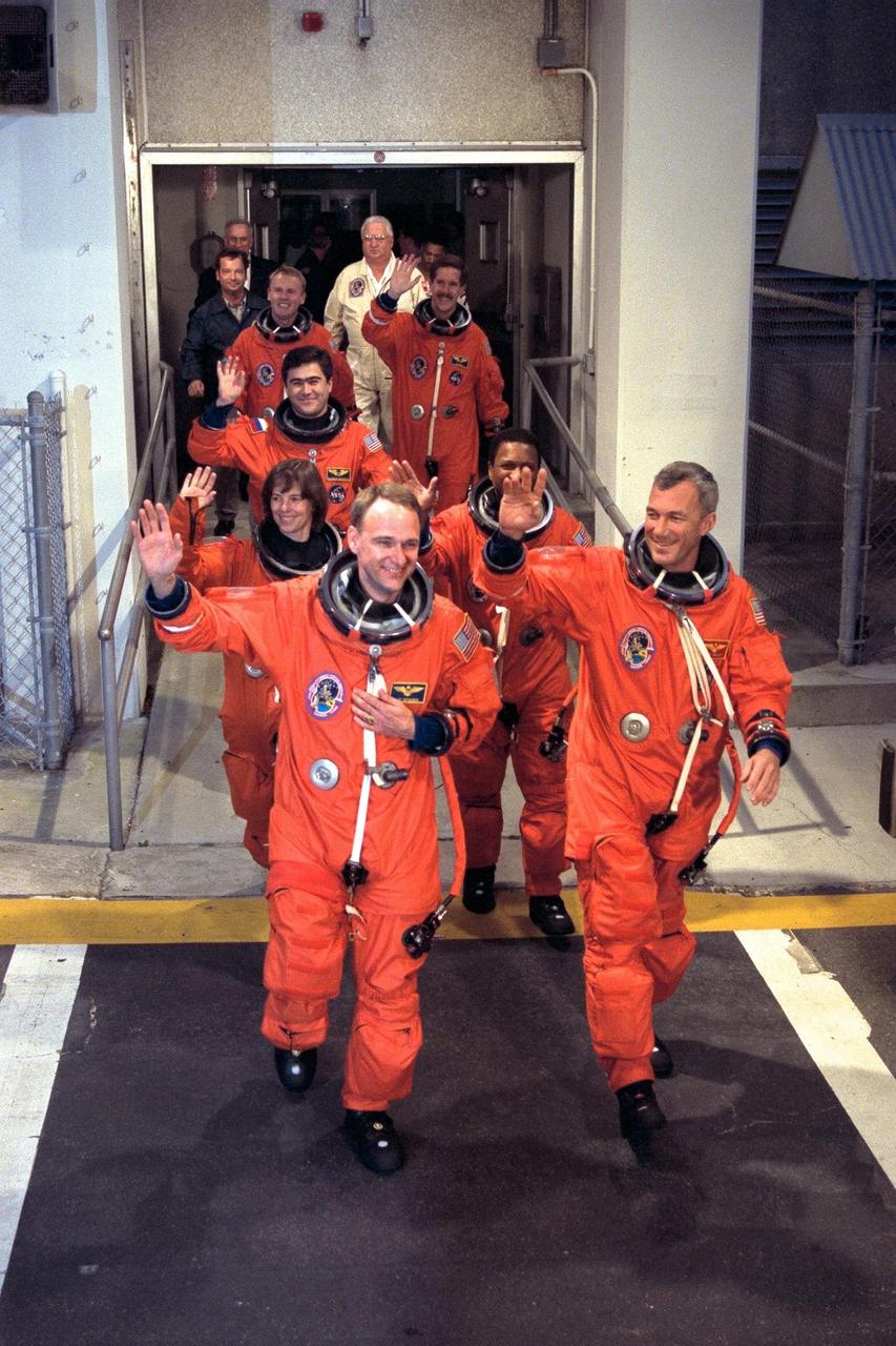 The STS-89 crew walk out of the Operations and Checkout Building and head for the Astrovan that will transport them to Launch Pad 39A, where the Space Shuttle Endeavour awaits to take them to Russia’s Mir space station. Waving to the crowd and leading the way, from front to back, left to right, are Pilot Joe Edwards Jr., Commander Terrence Wilcutt, and Mission Specialists Bonnie Dunbar, Ph.D., Michael Anderson, Salizhan Sharipov of the Russian Space Agency, Andrew Thomas, Ph.D., and James Reilly, Ph.D. STS-89, slated for a 9:48 p.m. EST liftoff Jan. 22, is the eighth docking with the Russian Space Station Mir, the first Mir docking for Endeavour (all previous dockings were made by Atlantis), and the first launch of 1998. After docking with Mir, Mission Specialist Andrew Thomas, Ph.D., will transfer to the space station, succeeding David Wolf, M.D