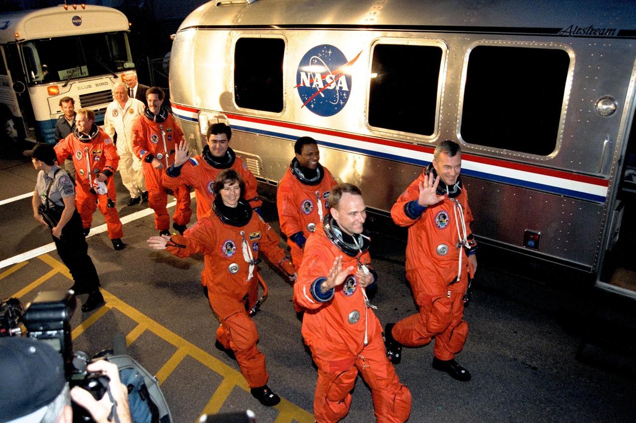 The STS-89 crew walk out of the Operations and Checkout Building and head for the Astrovan that will transport them to Launch Pad 39A, where the Space Shuttle Endeavour awaits to take them to Russia’s Mir space station. Waving to the crowd and leading the way, from front to back, left to right, are Pilot Joe Edwards Jr., Commander Terrence Wilcutt, and Mission Specialists Bonnie Dunbar, Ph.D., Michael Anderson, Salizhan Sharipov of the Russian Space Agency, Andrew Thomas, Ph.D., and James Reilly, Ph.D. STS-89, slated for a 9:48 p.m. EST liftoff Jan. 22, is the eighth docking with the Russian Space Station Mir, the first Mir docking for Endeavour (all previous dockings were made by Atlantis), and the first launch of 1998. After docking with Mir, Mission Specialist Andrew Thomas, Ph.D., will transfer to the space station, succeeding David Wolf, M.D