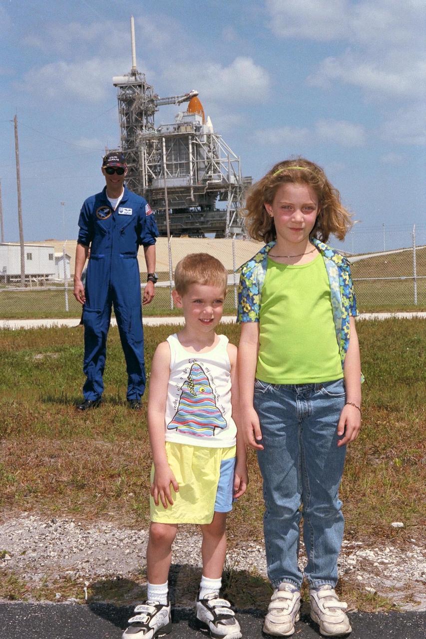 STS-90 Payload Specialist James Pawelczyk, Ph.D., stands behind his two children, Bradley and Katlyn (left to right), as they smile to photographers near Launch Pad 39B. James and the rest of the seven-member crew are scheduled to launch aboard Columbia, seen in the background, on May 16 at 2:19 p.m. EDT. The astronauts are under strict health stabilization guidelines to protect them from close contact with persons who do not have health stabilization clearance. This is the 25th flight of Columbia and the 90th mission flown since the start of the Space Shuttle program. This launch of Neurolab will examine the effects of spaceflight on the brain, spinal cord, peripheral nerves and sensory organs in the human body
