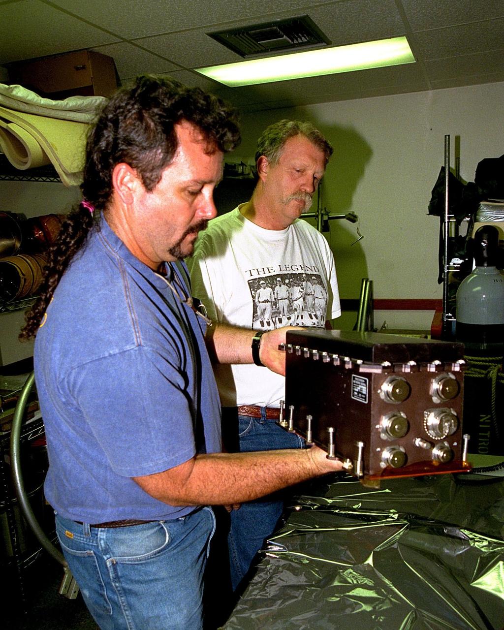KENNEDY SPACE CENTER, FLA. -- Two USA employees, Tim Seymour (at left) and Danny Brown (at right), look at the network signal processor (NSP) that was responsible for postponement of the launch of STS-90 on Apr. 16. The Space Shuttle Columbia's liftoff from Launch Pad 39B was postponed 24 hours due to difficulty with NSP No. 2 on the orbiter. This device formats data and voice communications between the ground and the Space Shuttle. The unit, which is located in the orbiter's mid-deck, was removed and replaced on Apr. 16. Mission managers first noticed the problem at about 3 a.m. during normal communications systems activation prior to tanking operations. As a result, work to load the external tank with the cryogenic propellants did not begin and launch postponement was made official at about 8:15 a.m. STS-90 is slated to be the launch of Neurolab, a nearly 17-day mission to examine the effects of spaceflight on the brain, spinal cord, peripheral nerves and sensory organs in the human body.