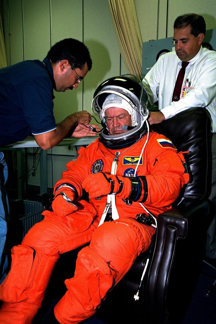 STS-91 Mission Specialist and Russian cosmonaut Valery Victorovitch Ryumin is outfitted with his ascent/reentry flight suit and helmet by two suit technicians in the Operations and Checkout (O&C) Building. The final suit fitting and checkout takes place prior to the crew walkout and transport to Launch Pad 39A. He has been director of the Russian Shuttle-Mir program and flight director for the Salyut-7 and Mir space stations and is a veteran of three space flights with a total of 362 days in space. This will be Ryumin’s first visit to Mir. However, his experience with Russian spacecraft in orbit will prove extremely valuable as he helps the crew with Mir equipment transfer operations. He will also be assessing the condition of the station for the Russian space program. STS-91 is scheduled to be launched on June 2 with a launch window opening around 6:10 p.m. EDT. The mission will feature the ninth and final Shuttle docking with the Russian space station Mir, the first Mir docking for Discovery, the first on-orbit test of the Alpha Magnetic Spectrometer (AMS), and the first flight of the new Space Shuttle super lightweight external tank. Astronaut Andrew S. W. Thomas will return to Earth as a STS91 crew member after living more than four months aboard Mir