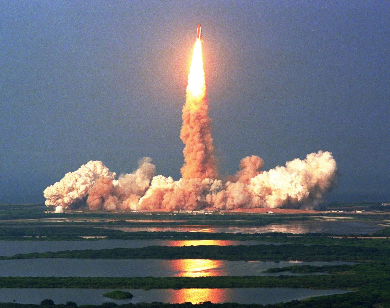 KENNEDY SPACE CENTER,  Fla. -- The abundance of water and marshes surrounding Launch Pad 39A becomes apparent from the vantage point of the Vehicle Assembly Building roof as the Space Shuttle Discovery lifts off at 6:06:24 p.m. EDT June 2. On board Discovery are Mission Commander Charles J. Precourt; Pilot Dominic L. Gorie; and Mission Specialists Wendy B. Lawrence, Franklin R. Chang-Diaz, Janet Lynn Kavandi and Valery Victorovitch Ryumin. The nearly 10-day mission will feature the ninth and final Shuttle docking with the Russian space station Mir, the first Mir docking for the Space Shuttle orbiter Discovery, the first on-orbit test of the Alpha Magnetic Spectrometer (AMS), and the first flight of the new Space Shuttle super lightweight external tank. Astronaut Andrew S. W. Thomas will be returning to Earth as an STS-91 crew member after living more than four months aboard Mir