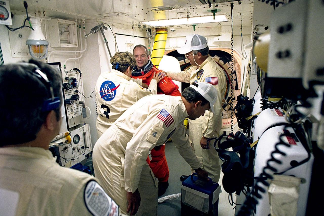 STS-91 Mission Commander Charles J. Precourt gets help with his flight gear from white room crew members Jean Alexander and Greg Lohning as he prepares to enter the Space Shuttle Discovery at Launch Pad 39A. White room crew member Dave Law is in the foreground