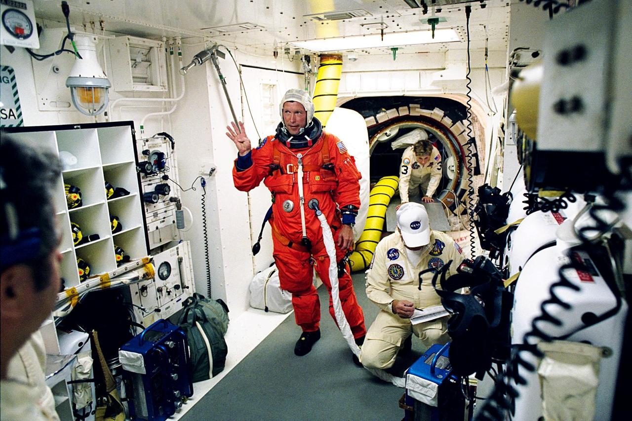 STS-91 Pilot Dominic L. Gorie waves to the camera as he is prepared for entry into the Space Shuttle Discovery by Launch Pad 39A white room crew members Jean Alexander (behind Gorie) and Greg Lohning