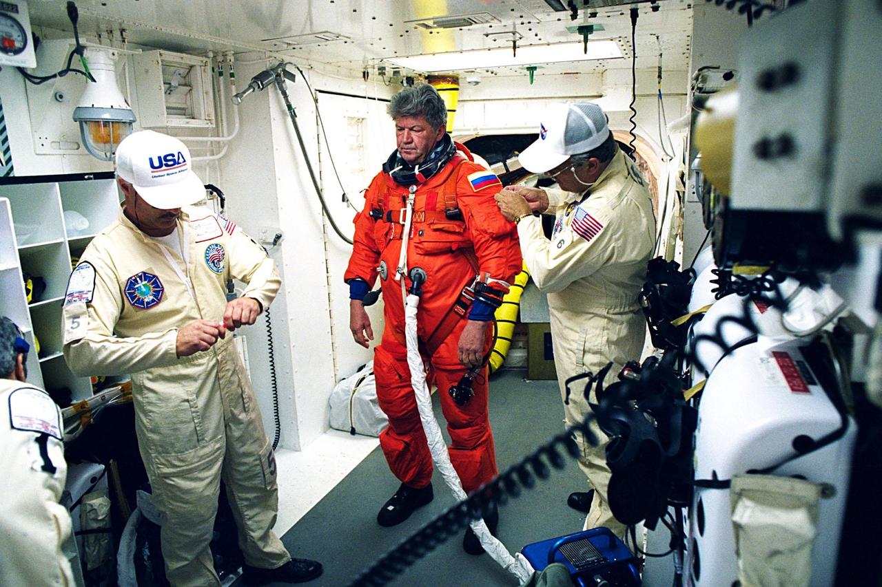 STS-91 Mission Specialist and Russian cosmonaut Valery Victorovitch Ryumin is assisted with his flight suit prior to his entry into the Space Shuttle Discovery by Launch Pad 39A white room crew members Chris Meinert (left) and Greg Lohning