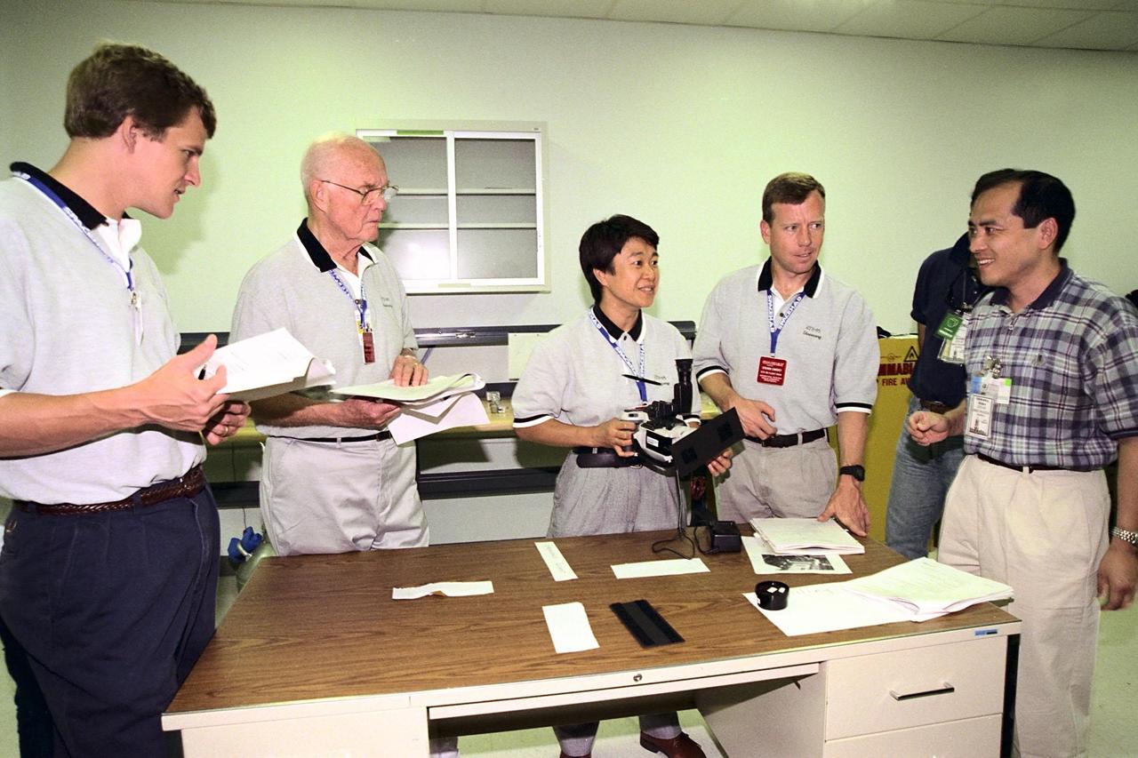 STS-95 crew members (from left) Mission Specialist Scott E. Parazynski, Payload Specialist John H. Glenn Jr., Payload Specialist Chiaki Mukai (with camera) representing the National Space Development Agency of Japan (NASDA), and Pilot Steven Lindsey listen to Hideo Ishikawa of NASDA, who explains some of the flight equipment at SPACEHAB Payload Processing Facility, Cape Canaveral, Fla. The STS-95 crew is at KSC to look at the SPACEHAB module and the equipment that will fly with them on the Space Shuttle Discovery, scheduled to launch Oct. 29, 1998. The mission includes research payloads such as the Spartan solar-observing deployable spacecraft, the Hubble Space Telescope Orbital Systems Test Platform, the International Extreme Ultraviolet Hitchhiker, as well as the SPACEHAB single module with experiments on space flight and the aging process
