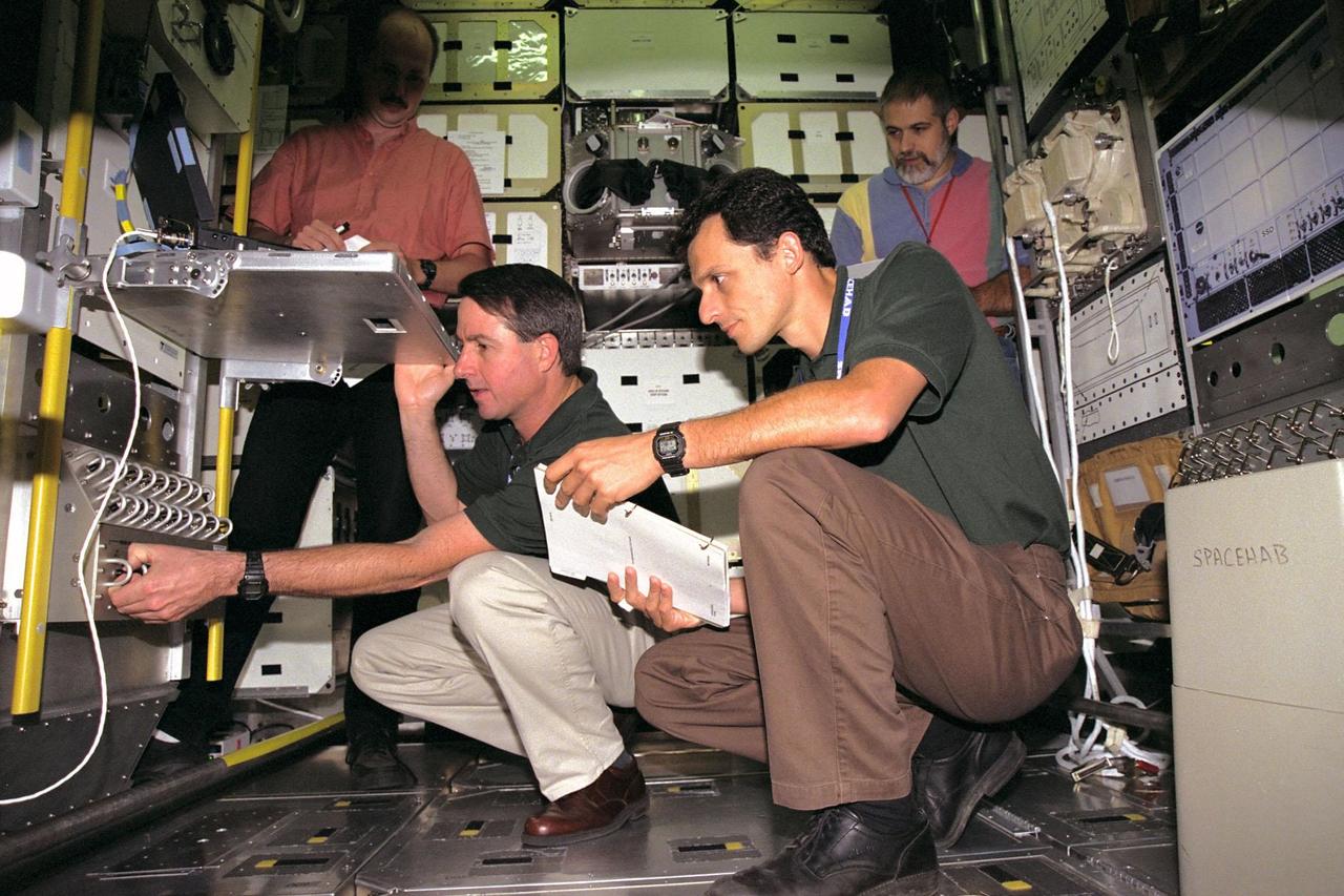 KENNEDY SPACE CENTER, FLA. -- While workers look on, STS-95 Mission Specialists Stephen K. Robinson, kneeling at left, and Pedro Duque inspect equipment inside the SPACEHAB module trainer at the SPACEHAB Payload Processing Facility in Cape Canaveral. STS-95 will feature a variety of research payloads, including the Spartan solar-observing deployable spacecraft, the Hubble Space Telescope Orbital Systems Platform, the International Extreme Ultraviolet Hitchhiker, and experiments on space flight and the aging process. STS-95 is targeted for an Oct. 29 launch aboard the Space Shuttle Discovery