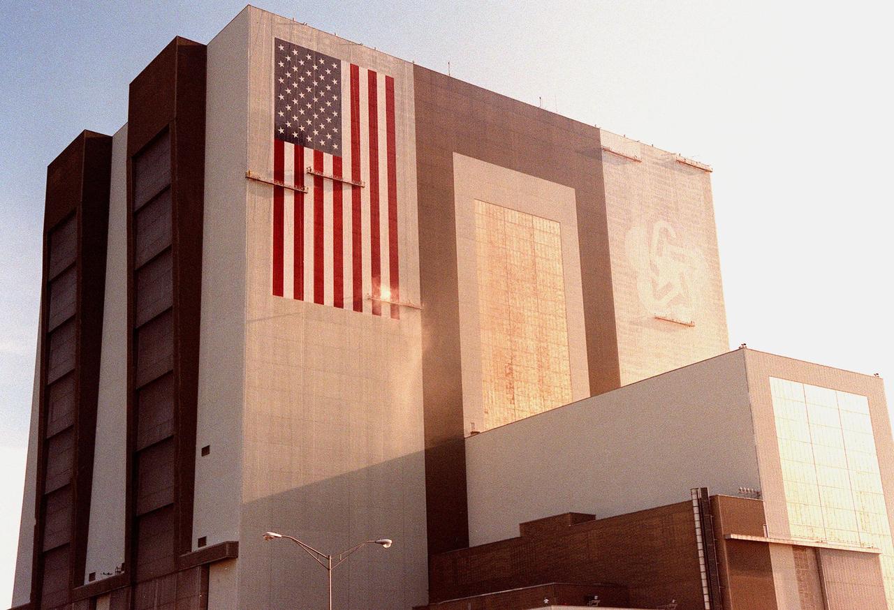 Painters are suspended on platforms from the top of the 525-foot-high Vehicle Assembly Building (VAB) at KSC during repainting of the American flag and NASA logo. The flag spans an area 209 feet by 110 feet and will require 510 gallons of red, white and blue paint. Each stripe of the flag is 9 feet wide and each star is 6 feet in diameter. The previous Bicentennial Emblem on the other side of the VAB doors is being replaced by the NASA logo, honoring NASA’s 40th anniversary (in October). The logo covers an area 110 feet by 132 feet. The painting platforms are operated by two electric motors and travel 35 feet per minute. Work is being done with rollers, with brushes being used for details. The paint was donated by ICI Devoe of Louisville, Ky. Work is expected to be completed in mid-September