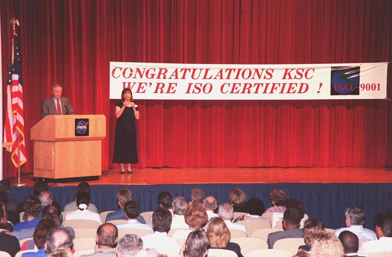 Center Director Roy Bridges speaks to KSC employees at the ISO certification ceremony held at the Training Auditorium. Bridges was presented an ISO 9001 certificate and plaque awarded to KSC by Det Norske Veritas (DNV), Inc., an international ISO certification organization. ISO 9001 comprises the most detailed, comprehensive set of standard requirements for quality programs established by the International Standards Organization. The presentation followed a successful independent audit by DNV of the KSC Management System in May of this year. The third-party auditors examined about 20 elements of KSC's system, including management responsibility, design control, documentation, test and inspection, and corrective action procedures. DNV found that KSC met or exceeded the stringent quality standards in all areas. KSC will use this certification as a tool to improve an already worldclass team. All NASA centers are required by NASA Administrator Daniel S. Goldin to be ISO 9001 registered by September 1999. NASA is the first federal agency to seek the quality certification. Next to Bridges is Heidi Hollingsworth, with the Center for Independent Living, who uses American Sign Language for any hearing-impaired employees in the audience