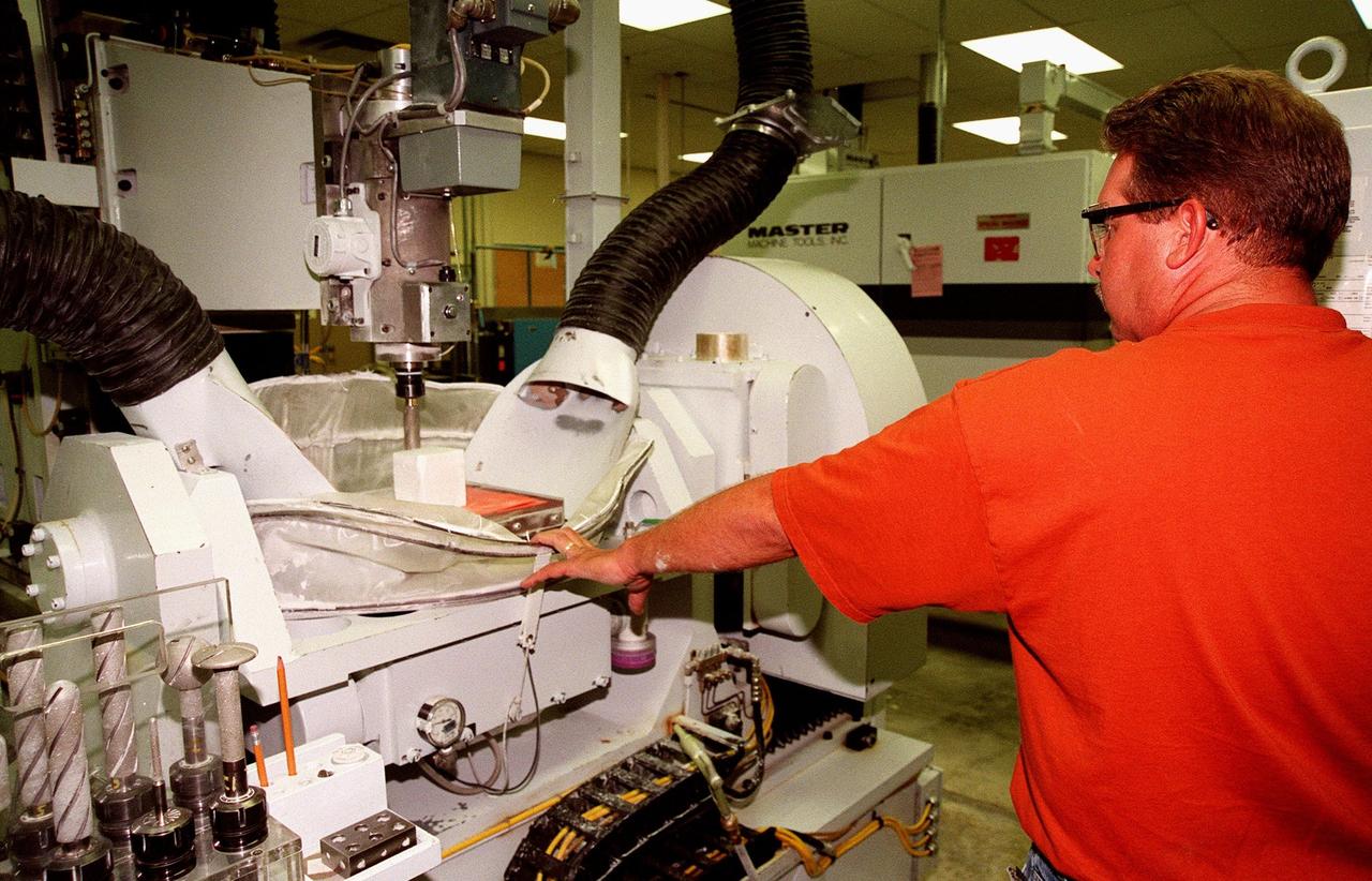 In the Tile Fabrication Shop, Tony Rollins, with United Space Alliance, holds down a curtain while making a test sample of tile on a block 5-axis computerized numerical control milling machine. About 70 percent of a Space Shuttle orbiter’s external surface is shielded from heat by a network of more than 24,000 tiles formed from a silica fiber compound. They are known as High-Temperature Reusable Surface Insulation (HRSI) tiles and Low-Temperature Reusable Surface Insulation (LRSI) tiles. Most HRSI tiles are 6 inches square, but may be as large as 12 inches in some areas, and 1 to 5 inches thick. LRSI tiles are generally 8 inches square, ranging from 0.2to 1-inch thick. More advanced materials such as Flexible Insulation Blankets have replaced tiles on some upper surfaces of the orbiter