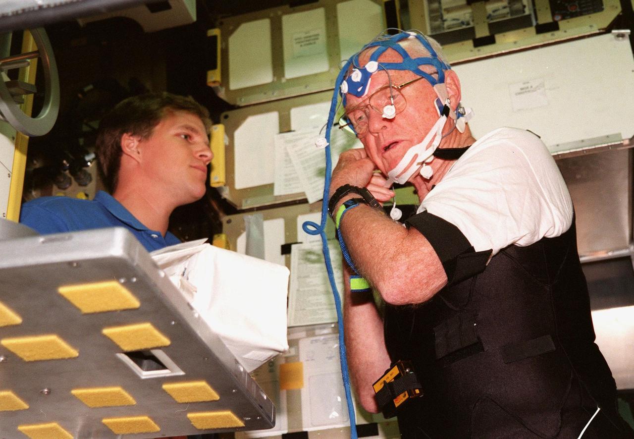 KENNEDY SPACE CENTER, FLA. -- Inside the SPACECHAB training module, STS-95 Payload Specialist John Glenn, who is a senator from Ohio, tries on the mesh cap that he will wear on the mission to monitor and record brain waves during sleep. Mission Specialist Scott Parazynski, M.D., watches. Parazynski and Glenn are participating in SPACEHAB familiarization at the SPACEHAB Payload Processing Facility, Cape Canaveral. The mission, scheduled to launch Oct. 29, includes research payloads such as the Spartan solar-observing deployable spacecraft, the Hubble Space Telescope Orbital Systems Test Platform, the International Extreme Ultraviolet Hitchhiker, as well as the SPACEHAB single module with experiments on space flight and the aging process