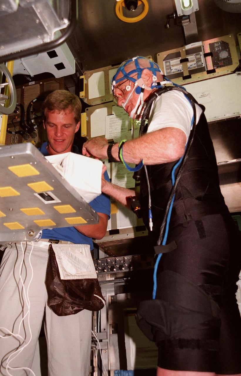 KENNEDY SPACE CENTER, FLA. -- Inside the SPACEHAB training module, STS-95 Mission Specialist Scott Parazynski, M.D., helps adjust connections for the mesh cap and the Respiratory Inductance Plethysmograph (RIP) suit worn by Payload Specialist John Glenn, who is a senator from Ohio. The cap and suit, which Glenn will wear on the mission, are part of the equipment that will be used to seek to improve the quality of sleep for future astronauts. The STS-95 crew are participating in SPACEHAB familiarization at the SPACEHAB Payload Processing Facility, Cape Canaveral. The mission, scheduled to launch Oct. 29, includes research payloads such as the Spartan solar-observing deployable spacecraft, the Hubble Space Telescope Orbital Systems Test Platform, the International Extreme Ultraviolet Hitchhiker, as well as the SPACEHAB single module with experiments on space flight and the aging process