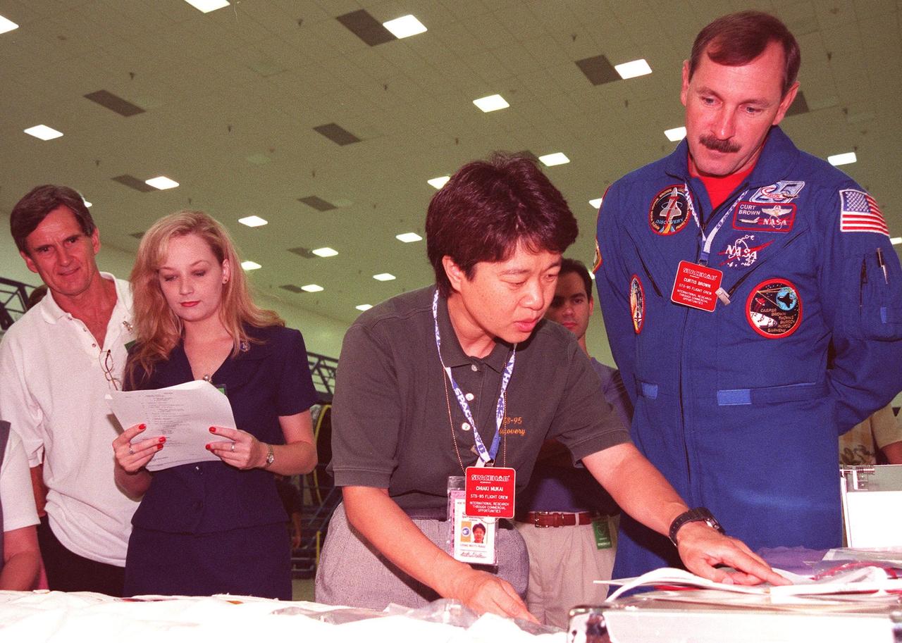 KENNEDY SPACE CENTER, FLA. -- STS-95 Payload Specialist Chiaki Mukai (center), representing the National Space Development Agency of Japan (NASDA) and Mission Commander Curtis L. Brown Jr. review equipment and documentation for the SPACEHAB at the SPACEHAB Payload Processing Facility (SPPF), Cape Canaveral. Onlookers behind them provide support. The STS-95 crew are participating in SPACEHAB familiarization at the SPPF. The mission, scheduled to launch Oct. 29, includes research payloads such as the Spartan solar-observing deployable spacecraft, the Hubble Space Telescope Orbital Systems Test Platform, the International Extreme Ultraviolet Hitchhiker, as well as the SPACEHAB single module with experiments on space flight and the aging process