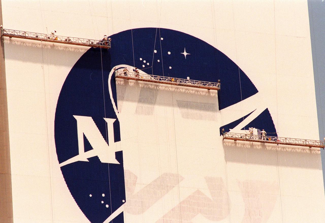 KENNEDY SPACE CENTER, FLA. -- The NASA logo, also known as the "meatball," is painted on the side of the Vehicle Assembly Building (VAB). When finished, the logo will measure 110 feet by 132 feet, or about 12,300 square feet. Workers, suspended on platforms from the top of the 525-foot-high VAB, are using rollers and brushes to do the painting. In addition to the logo, the American flag is also being repainted on the other side of the VAB. The flag spans an area 209 feet by 110 feet, or about 23, 437 square feet. Each stripe is 9 feet wide and each star is 6 feet in diameter. The entire fleet of orbiters is also receiving the addition of the NASA logo on their wings and sidewalls. The painting honors NASA’s 40th anniversary on Oct. 1 and is expected to be complete in mid-September