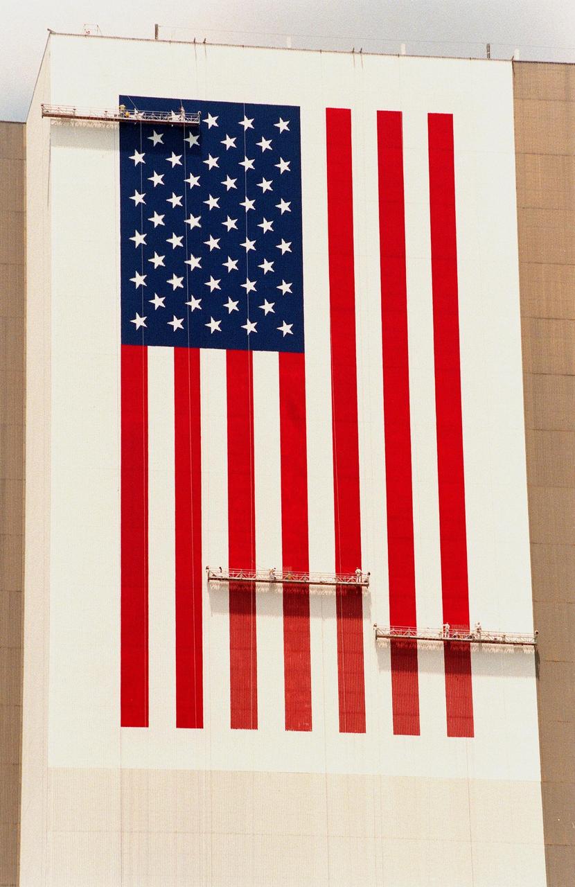 KENNEDY SPACE CENTER, FLA. -- The American flag is being repainted on the side of the Vehicle Assembly Building (VAB). The flag spans an area 209 feet by 110 feet, or about 23, 437 square feet. Each stripe is 9 feet wide and each star is 6 feet in diameter. Workers, suspended on platforms from the top of the 525-foot-high VAB, are using rollers and brushes to do the painting. In addition to the flag, the NASA logo, also known as the "meatball," is being painted on the VAB. When finished, the logo will measure 110 feet by 132 feet, or about 12,300 square feet. The entire fleet of orbiters is also receiving the addition of the NASA logo on their wings and sidewalls. The painting honors NASA’s 40th anniversary on Oct. 1 and is expected to be complete in mid-September