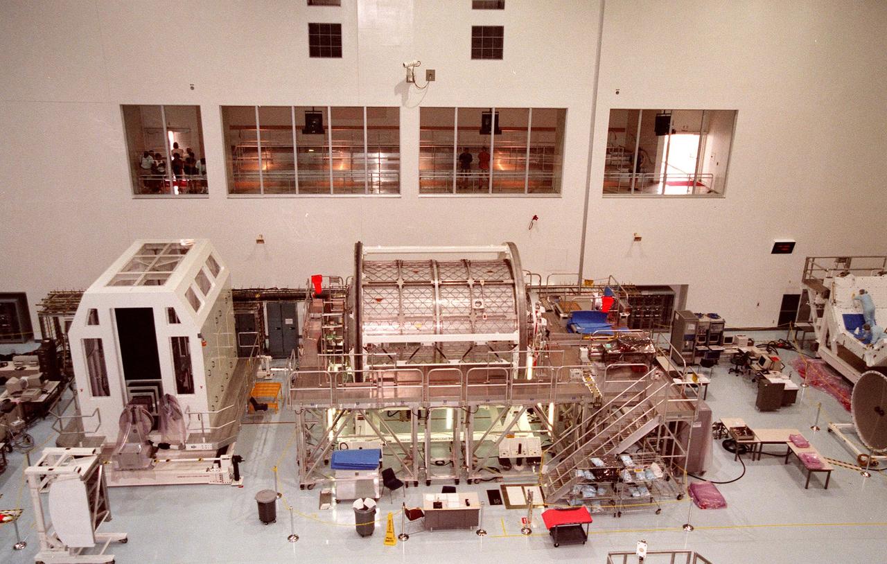(Center) The Multi-Purpose Launch Module, named Leonardo, awaits processing in the Space Station Processing Facility (SSPF). At left is a Rack Insertion Device. Above the Leonardo are the windows of the tour room where visitors can watch the activities in the SSPF. Scheduled to be launched on STS-100 on Dec. 2, 1999, the Italian-built MPLM will be carried in the payload bay of the Shuttle orbiter, and will provide storage and additional work space for up to two astronauts when docked to the International Space Station. The Leonardo is the first of three modules being provided by Alenia Aerospazio. The second MPLM, to be handed over in April 1999, is named Raffaello. A third module, to be named Donatello, is due to be delivered in October 2000 for launch in January 2001