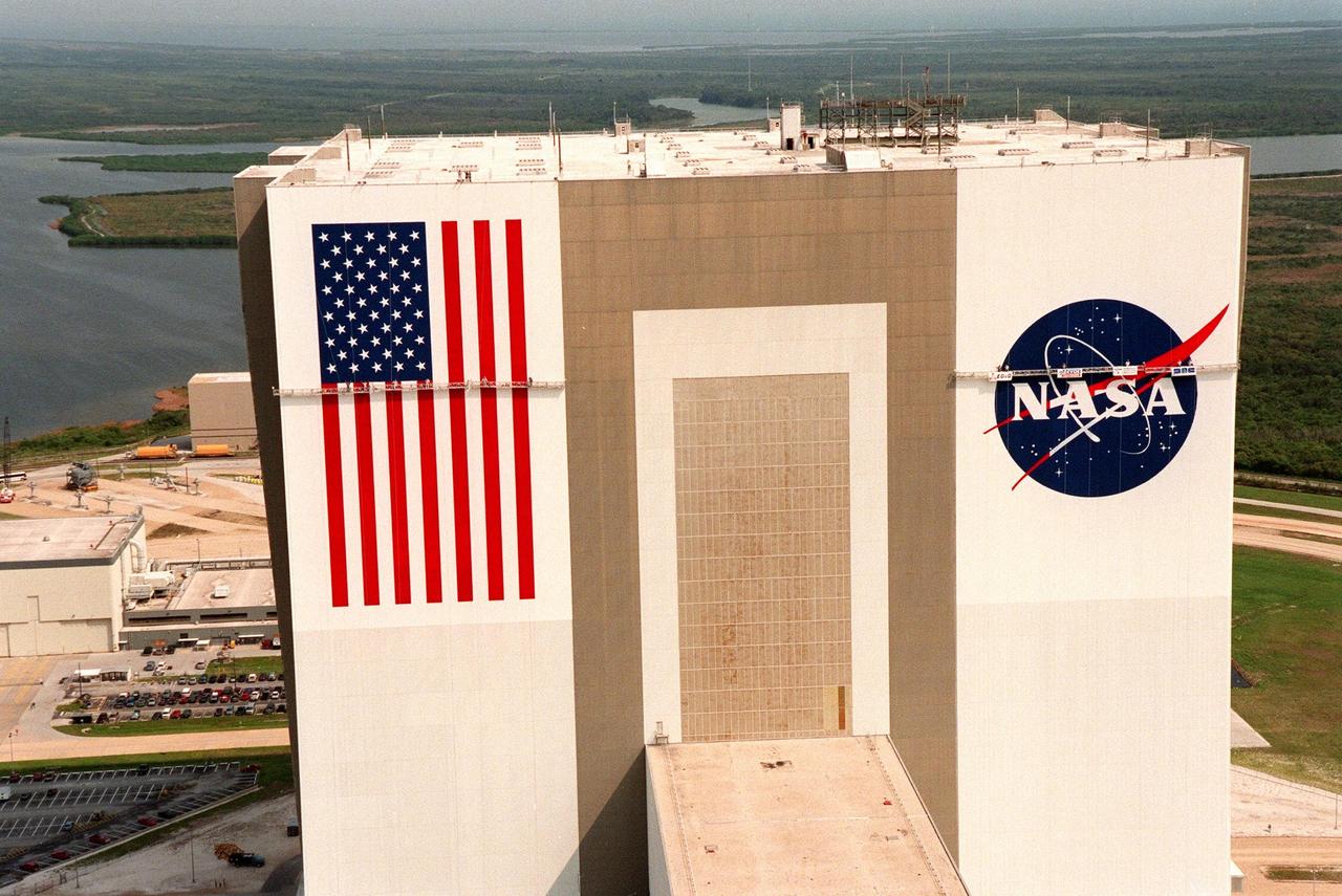 KENNEDY SPACE CENTER, FLA. -- This aerial view shows the Vehicle Assembly Building (VAB) getting a facelift with the repainting of the American flag and replacing of the Bicentennial emblem with the NASA logo. The painting honors NASA's 40th anniversary on Oct. 1 and is expected to be complete in mid-September. The flag spans an area 209 feet by 110 feet, or about 23,437 square feet. Each stripe is 9 feet wide and each star is 6 feet in diameter. The logo, also known as the "meatball," measures 110 feet by 132 feet, or about 12,300 square feet. Workers, suspended on platforms from the top of the 525-foot-high VAB, are using rollers and brushes to do the painting. The entire fleet of orbiters is also receiving the addition of the NASA logo on their wings and sidewalls