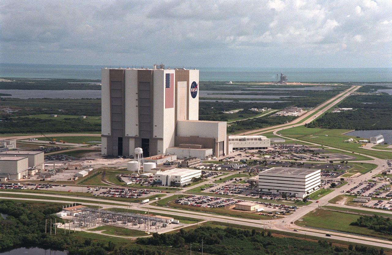 An aerial view of Launch Complex 39 area shows the Vehicle Assembly Building (center), with the Launch Control Center on its right. On the west side (lower end) are (left to right) the Orbiter Processing Facility, Process Control Center and Operations Support Building. Looking east (upper end) are Launch Pads 39-A (right) and 39-B (just above the VAB). The crawlerway stretches between the VAB and the launch pads toward the Atlantic Ocean, seen beyond them. At right is the turn basin where new external tanks are brought via ship, shown at its offloading site.