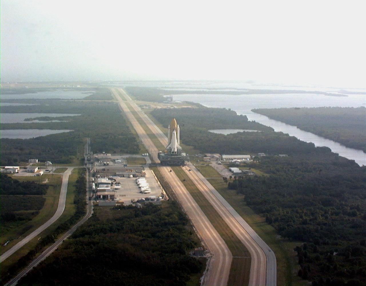 KENNEDY SPACE CENTER, FLA. -- Under low clouds and fog, Space Shuttle Discovery makes its trek along the stretch of crawlerway between the Vehicle Assembly Building and Launch Pad 39B atop the mobile launcher platform and crawler transporter. Once at the pad, the orbiter, external tank and solid rocket boosters will undergo final preparations for the STS-103 launch targeted for Dec. 6, 1999, at 2:37 a.m. EST. The mission is a "call-up" due to the need to replace portions of the pointing system the gyros which have begun to fail on the Hubble Space Telescope. Although Hubble is operating normally and conducting its scientific observations, only three of its six gyroscopes are working properly. The gyroscopes allow the telescope to point at stars, galaxies and planets. The STS-103 crew will also be installing a Fine Guidance Sensor, a new enhanced computer, a solid-state digital recorder, and a new spare transmitter to replace older equipment, and replacing degraded insulation on the telescope with new thermal insulation. The crew will also install a Battery Voltage/Temperature Improvement Kit to protect the spacecraft batteries from overcharging and overheating when the telescope goes into a safe mode. Four EVA's are planned to make the necessary repairs and replacements on the telescope. The STS-103 crew members are Commander Curtis L. Brown Jr., Pilot Scott J. Kelly, Mission Specialist Steven L. Smith, Mission Specialist C. Michael Foale (Ph.D.), Mission Specialist John M. Grunsfeld (Ph.D.), and Mission Specialist Claude Nicollier of Switzerland, and Mission Specialist Jean-François Clervoy of France, both with the European Space Agency