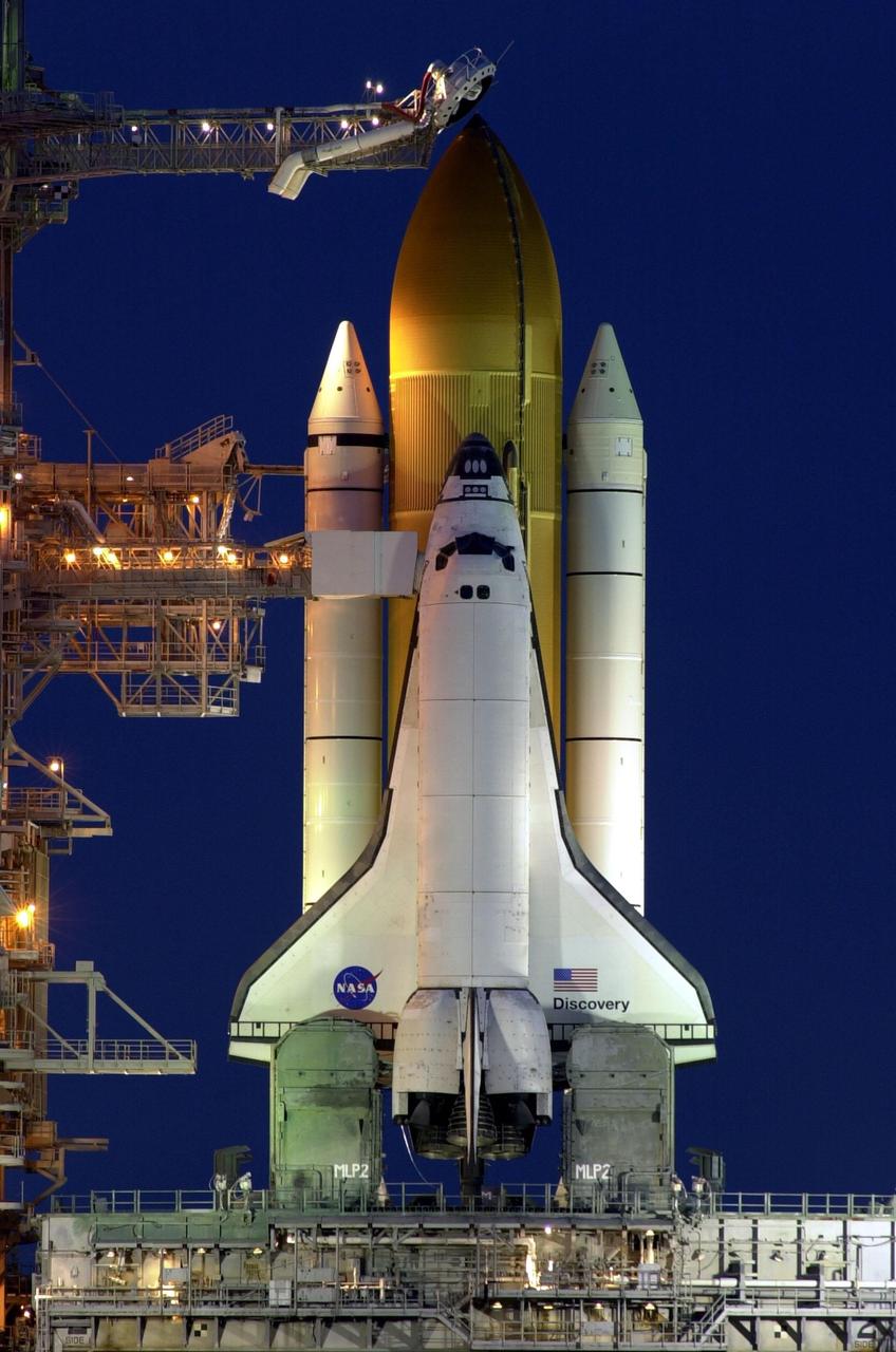 Just after sundown, Space Shuttle Discovery is framed with light from the Fixed Service Structure on Launch Pad 39B as it waits for liftoff on mission STS-103. At the top is seen the external tank gaseous oxygen vent arm system with the vent hood (commonly called the "beanie cap") poised above the external tank. The retractable arm and the beanie cap are designed to vent gaseous oxygen vapors away from the Space Shuttle. The arm truss section is 65 feet long and the diameter of the beanie cap is 13 feet. Extending toward the cabin of the orbiter is the orbiter access arm, with the environmental chamber (called the White Room) at the end. Through this chamber the crew enters the orbiter. The STS-103 mission, to service the Hubble Space Telescope, is scheduled for launch Dec. 17 at 8:47 p.m. EST. Mission objectives include replacing gyroscopes and an old computer, installing another solid state recorder, and replacing damaged insulation in the telescope. The mission is expected to last about 8 days and 21 hours. Discovery is expected to land at KSC Sunday, Dec. 26, at about 6:25 p.m. EST