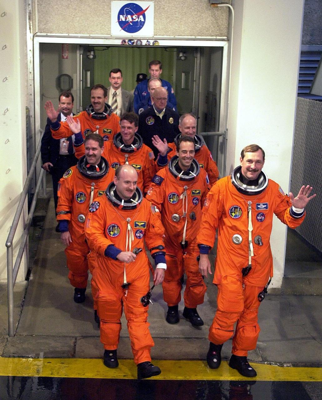 The STS-103 crew wave to onlookers as they walk out of the Operations and Checkout Building enroute to Launch Pad 39B and liftoff of Space Shuttle Discovery. In their orange launch and entry suits, they are (front row) Pilot Scott J. Kelly and Commander Curtis L. Brown Jr., (second row) Mission Specialists John M. Grunsfeld (Ph.D.) and Jean-Francois Clervoy of France, (third row) C. Michael Foale (Ph. D.) and Claude Nicollier of Switzerland, and bringing up the rear, Steven L. Smith. The STS-103 mission, to service the Hubble Space Telescope, is scheduled for launch Dec. 17 at 8:47 p.m. EST from Launch Pad 39B. Mission objectives include replacing gyroscopes and an old computer, installing another solid state recorder, and replacing damaged insulation in the telescope. After the 8-day, 21-hour mission, Discovery is expected to land at KSC Sunday, Dec. 26, at about 6:30 p.m. EST
