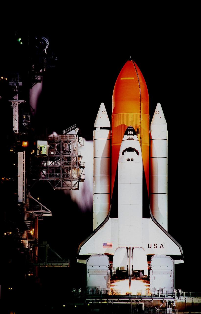 Moments before launch, sparks from the external ignitors are visible below the engines of Space Shuttle Columbia. The ignitors burn off a hydrogen concentration outside the orbiter near the main engines. A cloud effect behind the Shuttle's solid rocket booster and access arm to the left is created by spray from the water deluge system. The launch of STS-93 was scrubbed at the T-7 second mark in the countdown due to an indication of a high concentration of hydrogen in an aft engine compartment. The reading was proven to be a false alarm. The launch is rescheduled for July 22 at 12:28 a.m