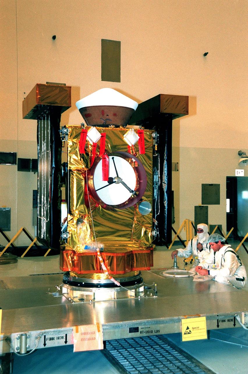 In the Payload Hazardous Servicing Facility, Casey McClellan (right), with Lockheed Martin, and an unidentified worker look over the spacecraft Stardust before a media presentation. Stardust is targeted for launch on Feb. 6 aboard a Boeing Delta II rocket from Launch Pad 17-A, Cape Canaveral Air Station. The spacecraft is destined for a close encounter with the comet Wild 2 in January 2004. Using a silicon-based substance called aerogel, Stardust will capture comet particles flying off the nucleus of the comet. The spacecraft also will bring back samples of interstellar dust. These materials consist of ancient pre-solar interstellar grains and other remnants left over from the formation of the solar system. Scientists expect their analysis to provide important insights into the evolution of the sun and planets and possibly into the origin of life itself. The collected samples will return to Earth in a sample return capsule (the white-topped, blunt-nosed cone seen on the top of the spacecraft) to be jettisoned as Stardust swings by Earth in January 2006