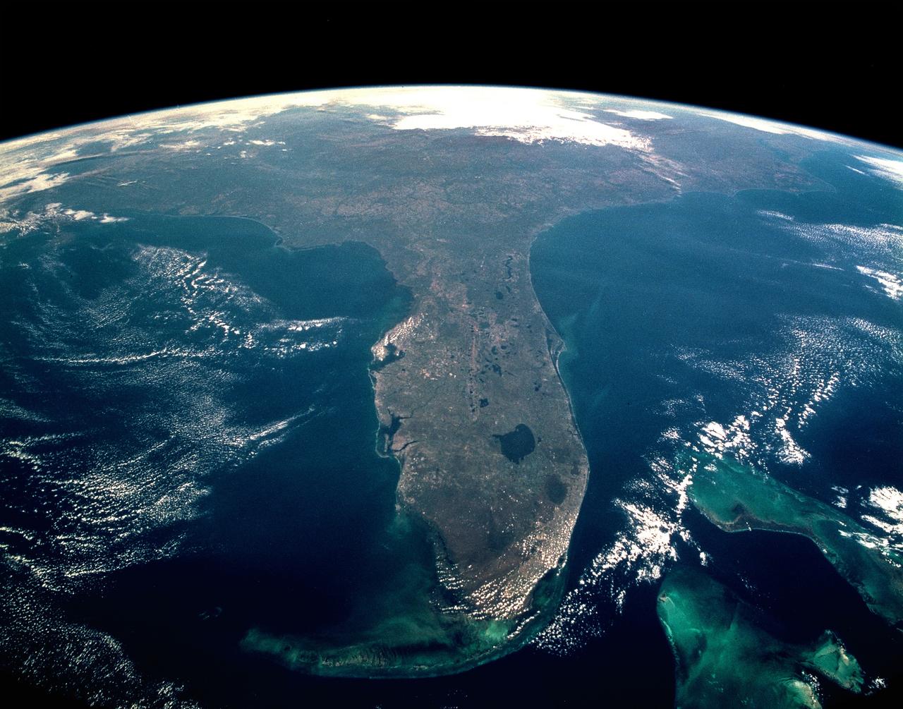 CAPE CANAVERAL, Fla. -- Taken during the STS-95 mission from a point over Cuba, this photo shows an oblique, foreshortened view of the Florida Peninsula, with the light blue, shallow seafloor of both the Florida Keys (curving across the bottom of the view) and the Bahama banks (right). "Popcorn" cumulus cloud covers Miami and the Southern Everglades, although the built-up area from Ft. Lauderdale to West Palm Beach can be discerned. Lake Okeechobee is the prominent waterbody in Florida. Cape Canaveral is shown well, half way up the peninsula. Orlando appears as the lighter patch West (left) of Cape Canaveral, near the middle of the peninsula. Cape Hatteras appears top right, with the North part of Chesapeake Bay also visible. This is a visibility of 16 degrees of latitude (23 degrees N over Cuba to 39 degrees at Baltimore), showing unusual atmospheric clarity.