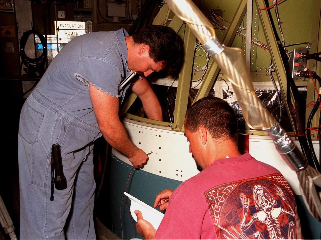 At Launch Pad 17-A, Cape Canaveral Air Station, a worker (left) runs a wire through a mounting hole on the second stage of a Boeing Delta II rocket in order to affix an external video camera held by the worker at right. The Delta II will launch the Stardust spacecraft on Feb. 6. Looking toward Earth, the camera will record the liftoff and separation of the first stage. Stardust is destined for a close encounter with the comet Wild 2 in January 2004. Using a silicon-based substance called aerogel, Stardust will capture comet particles flying off the nucleus of the comet. The spacecraft also will bring back samples of interstellar dust. These materials consist of ancient pre-solar interstellar grains and other remnants left over from the formation of the solar system. Scientists expect their analysis to provide important insights into the evolution of the sun and planets and possibly into the origin of life itself. The collected samples will return to Earth in a sample return capsule to be jettisoned as Stardust swings by Earth in January 2006
