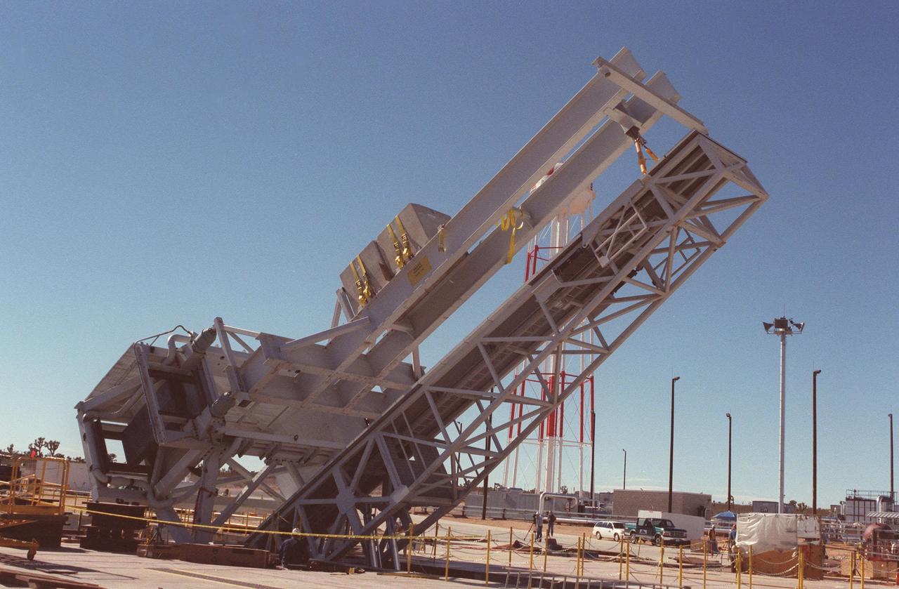 As part of X-33 launch equipment testing at Edwards Air Force Base, CA, the KSC-developed X-33 weight simulator (top), known as the "iron bird," is lifted to a vertical position at the X-33 launch site. The simulator matches the 75,000-pound weight and 63-foot height of the X-33 vehicle that will be using the launch equipment. KSC's Vehicle Positioning System (VPS) placed the simulator on the rotating launch platform prior to the rotation. The new VPS will dramatically reduce the amount of manual labor required to position a reusable launch vehicle for liftoff