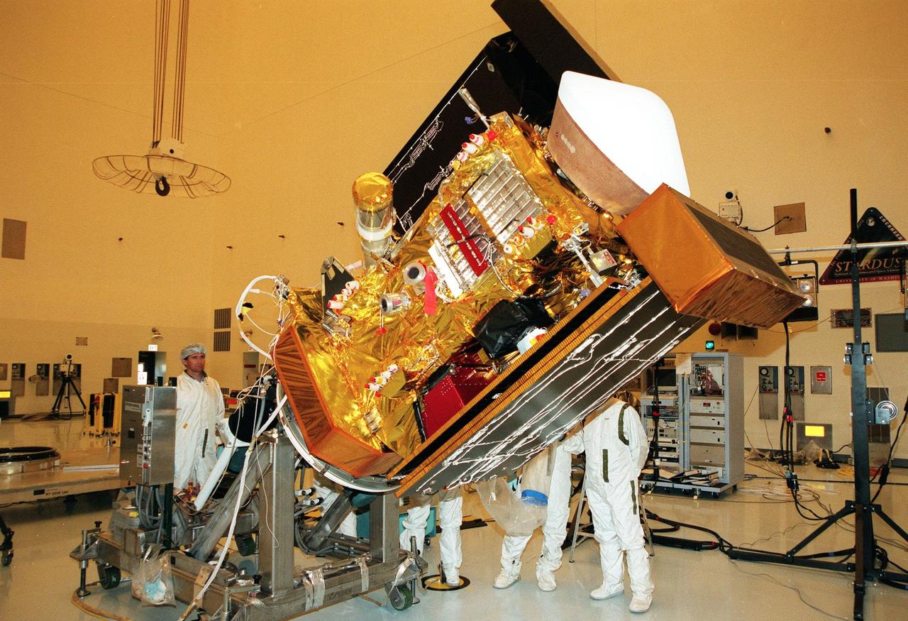 Workers in the Payload Hazardous Servicing Facility watch as the <a href="http://www-pao.ksc.nasa.gov/kscpao/captions/subjects/stardust.htm"> Stardust</a> spacecraft is lowered before deploying panels for lighting tests. Stardust is scheduled to be launched aboard a Boeing Delta II rocket from Launch Pad 17A, Cape Canaveral Air Station, on Feb. 6, 1999, for a rendezvous with the comet Wild 2 in January 2004. Stardust will use a substance called aerogel to capture comet particles flying off the nucleus of the comet, plus collect interstellar dust for later analysis. The collected samples will return to Earth in a sample return capsule (seen on top of the spacecraft) to be jettisoned as it swings by Earth in January 2006
