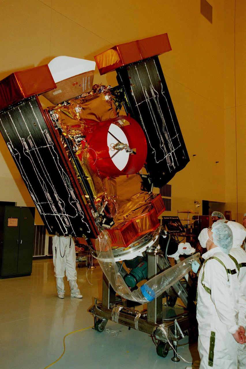 Workers in the Payload Hazardous Servicing Facility watch as the <a href="http://www-pao.ksc.nasa.gov/kscpao/captions/subjects/stardust.htm"> Stardust</a> spacecraft is rotated and lowered before deploying the solar panels for lighting tests. Stardust is scheduled to be launched aboard a Boeing Delta II rocket from Launch Pad 17A, Cape Canaveral Air Station, on Feb. 6, 1999, for a rendezvous with the comet Wild 2 in January 2004. Stardust will use a substance called aerogel to capture comet particles flying off the nucleus of the comet, plus collect interstellar dust for later analysis. The collected samples will return to Earth in a sample return capsule (seen on top of the spacecraft) to be jettisoned as it swings by Earth in January 2006