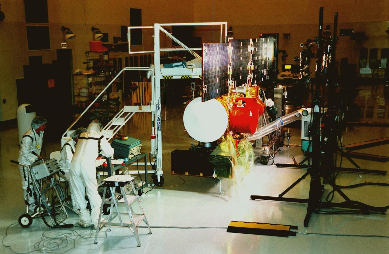 In the Payload Hazardous Servicing Facility, workers at left check instruments during a lighting test on the solar panels of the <a href="http://www-pao.ksc.nasa.gov/kscpao/captions/subjects/stardust.htm"> Stardust</a>spacecraft. Stardust is scheduled to be launched aboard a Boeing Delta II rocket from Launch Pad 17A, Cape Canaveral Air Station, on Feb. 6, 1999, for a rendezvous with the comet Wild 2 in January 2004. Stardust will use a substance called aerogel to capture comet particles flying off the nucleus of the comet, plus collect interstellar dust for later analysis. The collected samples will return to Earth in a sample return capsule (its white cap is seen on the near end of the spacecraft) to be jettisoned as it swings by Earth in January 2006