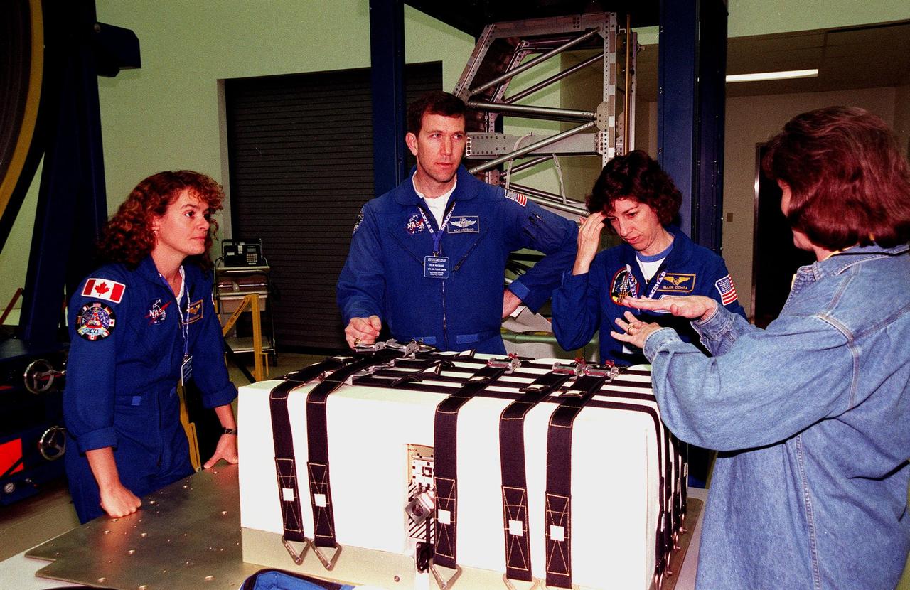 KENNEDY SPACE CENTER, FLA. -- In the SPACEHAB Facility, (from left) STS-96 Mission Specialist Julie Payette, Pilot Rick Husband and Mission Specialist Ellen Ochoa learn about the Sequential Shunt Unit (SSU) in front of them from Lynn Ashby (far right), with Johnson Space Center. The STS-96 crew is at KSC for a payload Interface Verification Test (IVT) for their upcoming mission to the International Space Station . Other crew members at KSC for the IVT are Commander Kent Rominger and Mission Specialists Tamara Jernigan, Dan Barry and Valery Tokarev of Russia. The SSU is part of the cargo on Mission STS-96, which carries the SPACEHAB Logistics Double Module, with equipment to further outfit the International Space Station service module and equipment that can be off-loaded from the early U.S. assembly flights. The SPACEHAB carries internal logistics and resupply cargo for station outfitting, plus an external Russian cargo crane to be mounted to the exterior of the Russian station segment and used to perform space walking maintenance activities. The double module stowage provides capacity of up to 10,000 lbs. with the ability to accommodate powered payloads, four external rooftop stowage locations, four double-rack locations (two powered), up to 61 bulkhead-mounted middeck locker locations, and floor storage for large unique items and Soft Stowage. STS-96 is targeted to launch May 20 about 9:32 a.m
