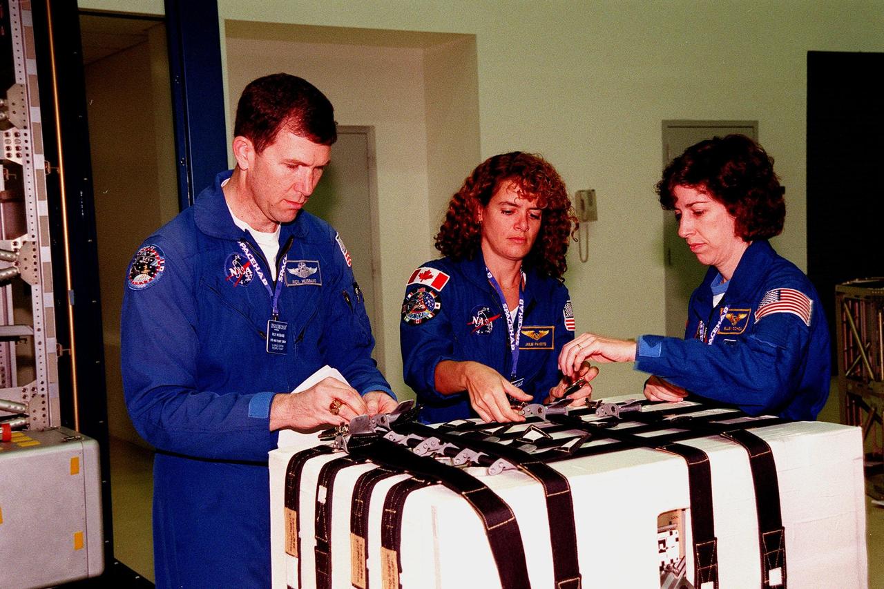 KENNEDY SPACE CENTER, FLA. -- In the SPACEHAB Facility, (left to right) STS-96 Pilot Rick Husband and Mission Specialists Julie Payette and Ellen Ochoa work the straps on the Sequential Shunt Unit (SSU) in front of them. The STS-96 crew is at KSC for a payload Interface Verification Test (IVT) for its upcoming mission to the International Space Station . Other crew members at KSC for the IVT are Commander Kent Rominger and Mission Specialists Tamara Jernigan, Dan Barry and Valery Tokarev of Russia. The SSU is part of the cargo on Mission STS-96, which carries the SPACEHAB Logistics Double Module, with equipment to further outfit the International Space Station service module and equipment that can be off-loaded from the early U.S. assembly flights. The SPACEHAB carries internal logistics and resupply cargo for station outfitting, plus an external Russian cargo crane to be mounted to the exterior of the Russian station segment and used to perform space walking maintenance activities. The double module stowage provides capacity of up to 10,000 lbs. with the ability to accommodate powered payloads, four external rooftop stowage locations, four double-rack locations (two powered), up to 61 bulkhead-mounted middeck locker locations, and floor storage for large unique items and Soft Stowage. STS-96 is targeted to launch May 20 about 9:32 a.m