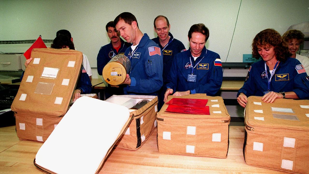KENNEDY SPACE CENTER, FLA. -- In the SPACEHAB Facility, the STS-96 crew looks at equipment as part of a payload Interface Verification Test (IVT) for their upcoming mission to the International Space Station . From left are Mission Specialist Ellen Ochoa (behind the opened storage cover ), Commander Kent Rominger, Pilot Rick Husband (holding a lithium hydroxide canister) and Mission Specialists Dan Barry, Valery Tokarev of Russia and Julie Payette. In the background is TTI interpreter Valentina Maydell. The other crew member at KSC for the IVT is Mission Specialist Tamara Jernigan. Mission STS-96 carries the SPACEHAB Logistics Double Module, which has equipment to further outfit the International Space Station service module and equipment that can be off-loaded from the early U.S. assembly flights. The SPACEHAB carries internal logistics and resupply cargo for station outfitting, plus an external Russian cargo crane to be mounted to the exterior of the Russian station segment and used to perform space walking maintenance activities. The double module stowage provides capacity of up to 10,000 lbs. with the ability to accommodate powered payloads, four external rooftop stowage locations, four double-rack locations (two powered), up to 61 bulkhead-mounted middeck locker locations, and floor storage for large unique items and Soft Stowage. STS-96 is targeted to launch May 20 about 9:32 a.m