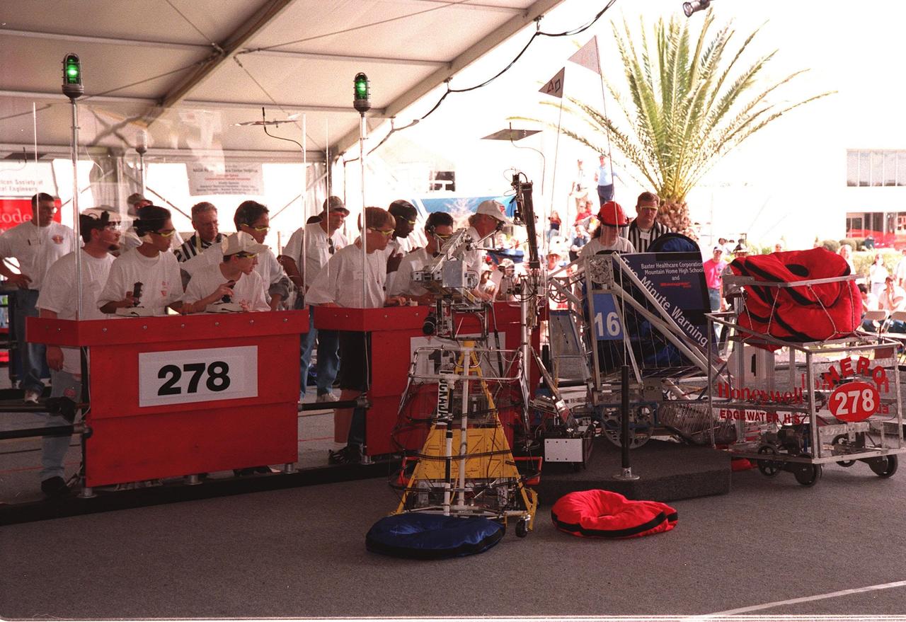 All four robots, maneuvered by student teams behind protective walls, converge on a corner of the playing field during qualifying matches of the 1999 Southeastern Regional robotic competition at Kennedy Space Center Visitor Complex . Thirty schools from around the country have converged at KSC for the event that pits gladiator robots against each other in an athletic-style competition. The robots have to retrieve pillow-like disks from the floor, as well as climb onto the platform (with flags) and raise the cache of pillows to a height of eight feet. KSC is hosting the event being sponsored by the nonprofit organization For Inspiration and Recognition of Science and Technology, known as FIRST. The FIRST robotics competition is designed to provide students with a hands-on, inside look at engineering and other professional careers