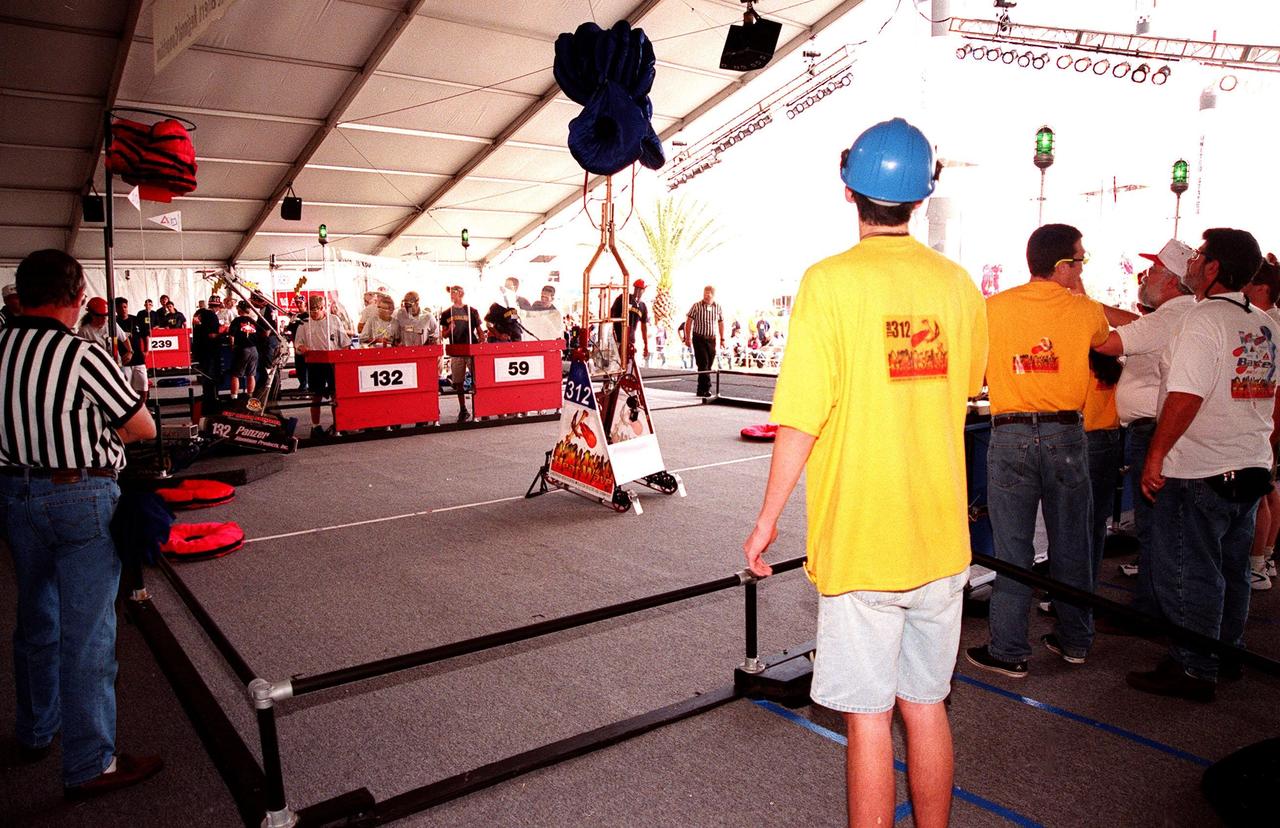 During final matches at the 1999 Southeastern Regional robotic competition at the KSC Visitor Complex, referees in opposite corners and student teams watch as two robots raise their pillow disks to a height of eight feet, one of the goals of the competition. Thirty schools from around the country have converged at KSC for the event that pits gladiator robots against each other in an athletic-style competition. The robots have to retrieve the pillow disks from the floor, climb onto a platform (with flags), as well as raise the cache of pillows, maneuvered by student teams behind protective walls. KSC is hosting the event being sponsored by the nonprofit organization For Inspiration and Recognition of Science and Technology, known as FIRST. The FIRST robotics competition is designed to provide students with a hands-on, inside look at engineering and other professional careers by pairing engineers and corporations with student teams