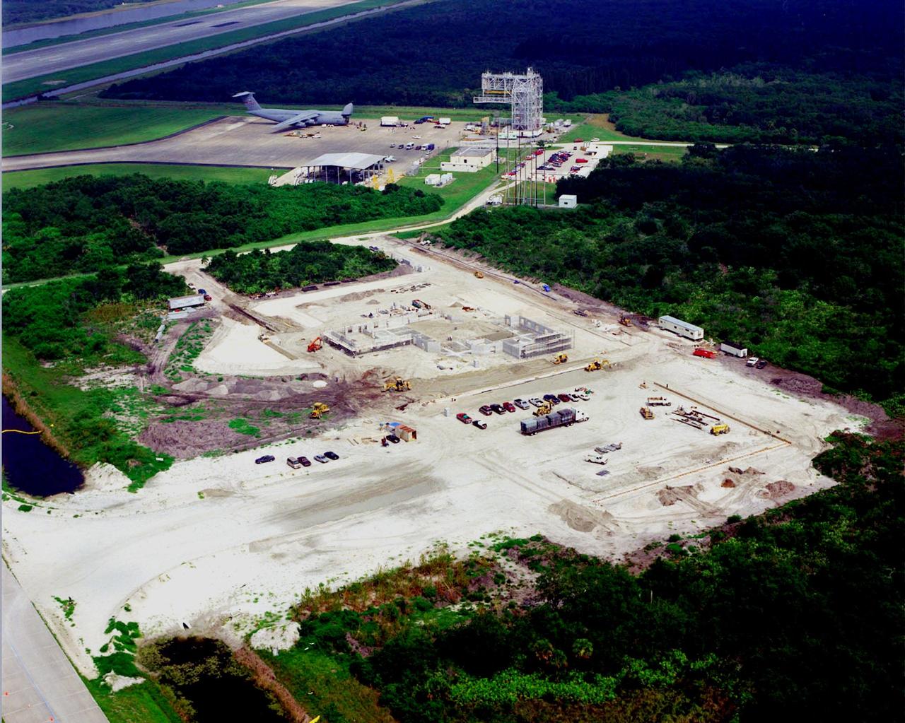 This aerial view shows the construction of a multi-purpose hangar, which is part of the $8 million Reusable Launch Vehicle (RLV) Support Complex at Kennedy Space Center. In the background is the Shuttle Landing Facility, with (left) a C-5 air cargo plane, the offloaded canister in front of it containing the Multi-Purpose Logistics Module Raffaello, and (right) the mate/demate tower that is used when an orbiter is transported to and from KSC atop a modified Boeing 747. The RLV complex will also include facilities for related ground support equipment and administrative/ technical support. It will be available to accommodate the Space Shuttle; the X-34 RLV technology demonstrator; the L-1011 carrier aircraft for Pegasus and X-34; and other RLV and X-vehicle programs. The complex is jointly funded by the Spaceport Florida Authority, NASA's Space Shuttle Program and KSC. The facility will be operational in early 2000. 