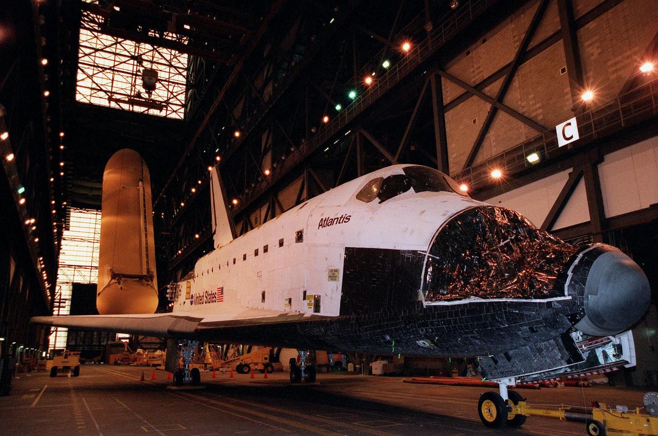 KENNEDY SPACE CENTER, FLA. -- In the transfer aisle of the Vehicle Assembly Building, Atlantis awaits a vacancy in one of the Orbiter Processing Facility bays. Seen behind the right wing is an external tank being raised to a vertical position. The largest and heaviest element of the Space Shuttle, an external tank contains the liquid hydrogen fuel and liquid oxygen oxidizer for the three Space Shuttle main engines (SSMEs) in the orbiter during liftoff and ascent. When the SSMEs are shut down, the external tank is jettisoned, breaking up as it enters the Earth's atmopshere and impacting in a remote ocean area. It is not recovered