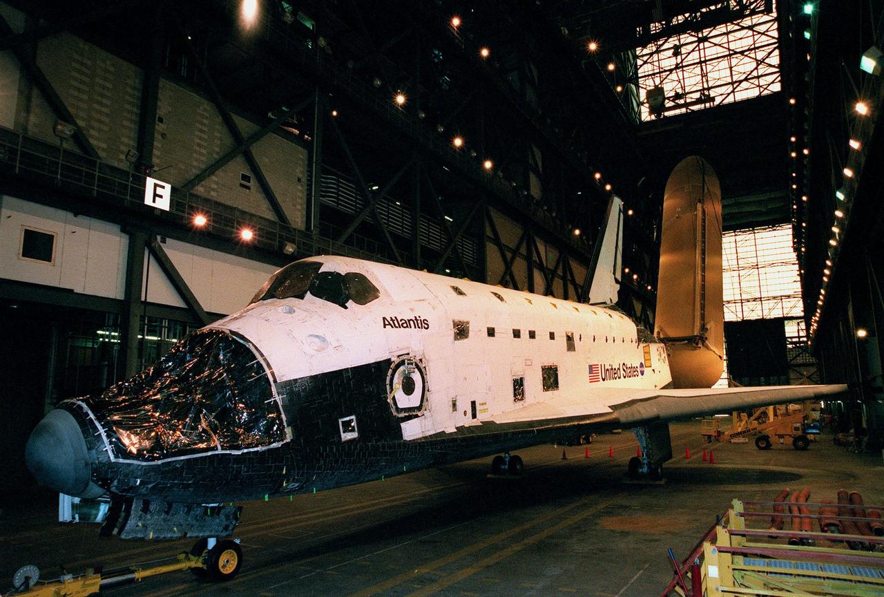 KENNEDY SPACE CENTER, FLA. -- In the transfer aisle of the Vehicle Assembly Building, Atlantis awaits a vacancy in one of the Orbiter Processing Facility bays. Seen behind the left wing is an external tank being raised to a vertical position. The largest and heaviest element of the Space Shuttle, an external tank contains the liquid hydrogen fuel and liquid oxygen oxidizer for the three Space Shuttle main engines (SSMEs) in the orbiter during liftoff and ascent. When the SSMEs are shut down, the external tank is jettisoned, breaking up as it enters the Earth's atmopshere and impacting in a remote ocean area. It is not recovered
