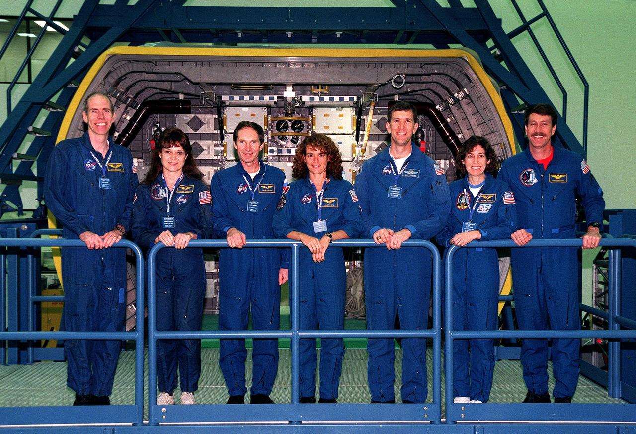 KENNEDY SPACE CENTER, FLA. -- Posing on the platform next to the SPACEHAB Logistics Double Module in the SPACEHAB Facility are the STS-96 crew (from left) Mission Specialists Dan Barry, Tamara Jernigan, Valery Tokarev of Russia, and Julie Payette; Pilot Rick Husband; Mission Specialist Ellen Ochoa; and Commander Kent Rominger. The crew is at KSC for a payload Interface Verification Test for their upcoming mission to the International Space Station. Mission STS-96 carries the SPACEHAB Logistics Double Module, which will have equipment to further outfit the International Space Station service module and equipment that can be off-loaded from the early U.S. assembly flights. It carries internal logistics and resupply cargo for station outfitting, plus an external Russian cargo crane to be mounted to the exterior of the Russian station segment and used to perform space walking maintenance activities. The double module stowage provides capacity of up to 10,000 lbs. with the ability to accommodate powered payloads, four external rooftop stowage locations, four double-rack locations (two powered), up to 61 bulkhead-mounted middeck locker locations, and floor storage for large unique items and Soft Stowage. STS-96 is targeted to launch May 20 about 9:32 a.m