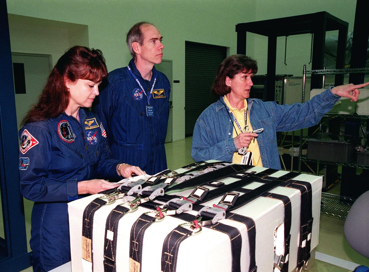 KENNEDY SPACE CENTER, FLA. -- During a payload Interface Verification Test (IVT) in the SPACEHAB Facility, STS-96 Mission Specialist Tamara Jernigan checks over instructions while Mission Specialist Dan Barry looks up from the Sequential Shunt Unit (SSU) in front of him to other equipment Lynn Ashby (right), with Johnson Space Center, is pointing at. Other crew members at KSC for the IVT are Commander Kent Rominger, Pilot Rick Husband, and Mission Specialists Ellen Ochoa, Julie Payette and Valery Tokarev of Russia. The SSU is part of the cargo on Mission STS-96, which carries the SPACEHAB Logistics Double Module, with equipment to further outfit the International Space Station service module and equipment that can be off-loaded from the early U.S. assembly flights. The SPACEHAB carries internal logistics and resupply cargo for station outfitting, plus an external Russian cargo crane to be mounted to the exterior of the Russian station segment and used to perform space walking maintenance activities. The double module stowage provides capacity of up to 10,000 lbs. with the ability to accommodate powered payloads, four external rooftop stowage locations, four double-rack locations (two powered), up to 61 bulkhead-mounted middeck locker locations, and floor storage for large unique items and Soft Stowage. STS-96 is targeted to launch May 20 about 9:32 a.m