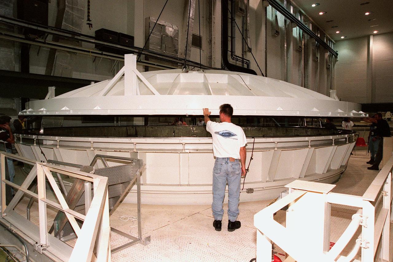 KENNEDY SPACE CENTER, FLA. -- Workers watch as the 27.5-ton lid is lowered onto the top of an altitude chamber in the Operations and Checkout Building high bay. The chamber was recently reactivated, after a 24-year hiatus, to perform leak tests on International Space Station pressurized modules at the launch site. Originally, two chambers were built to test Apollo Program flight hardware. They were last used in 1975 during the Apollo-Soyuz Test Project. After installation of new vacuum pumping equipment and controls, a new control room, and a new rotation handling fixture, the chamber again became operational in February 1999. The chamber, which is 33 feet in diameter and 50 feet tall, is constructed of stainless steel. The first module that will be tested for leaks is the U.S. Laboratory. No date has been determined for the test