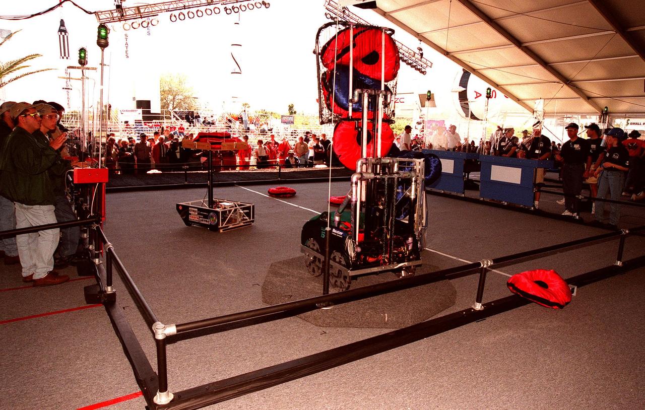 Student teams (right and left) behind protective walls maneuver their robots on the playing field during practice rounds of the 1999 Southeastern Regional robotic competition at Kennedy Space Center Visitor Complex . Thirty schools from around the country have converged at KSC for the event that pits gladiator robots against each other in an athletic-style competition. The robots have to retrieve pillow-like disks from the floor, as well as climb onto the platform (foreground) and raise the cache of pillows to a height of eight feet. KSC is hosting the event being sponsored by the nonprofit organization For Inspiration and Recognition of Science and Technology, known as FIRST. The FIRST robotics competition is designed to provide students with a hands-on, inside look at engineering and other professional careers