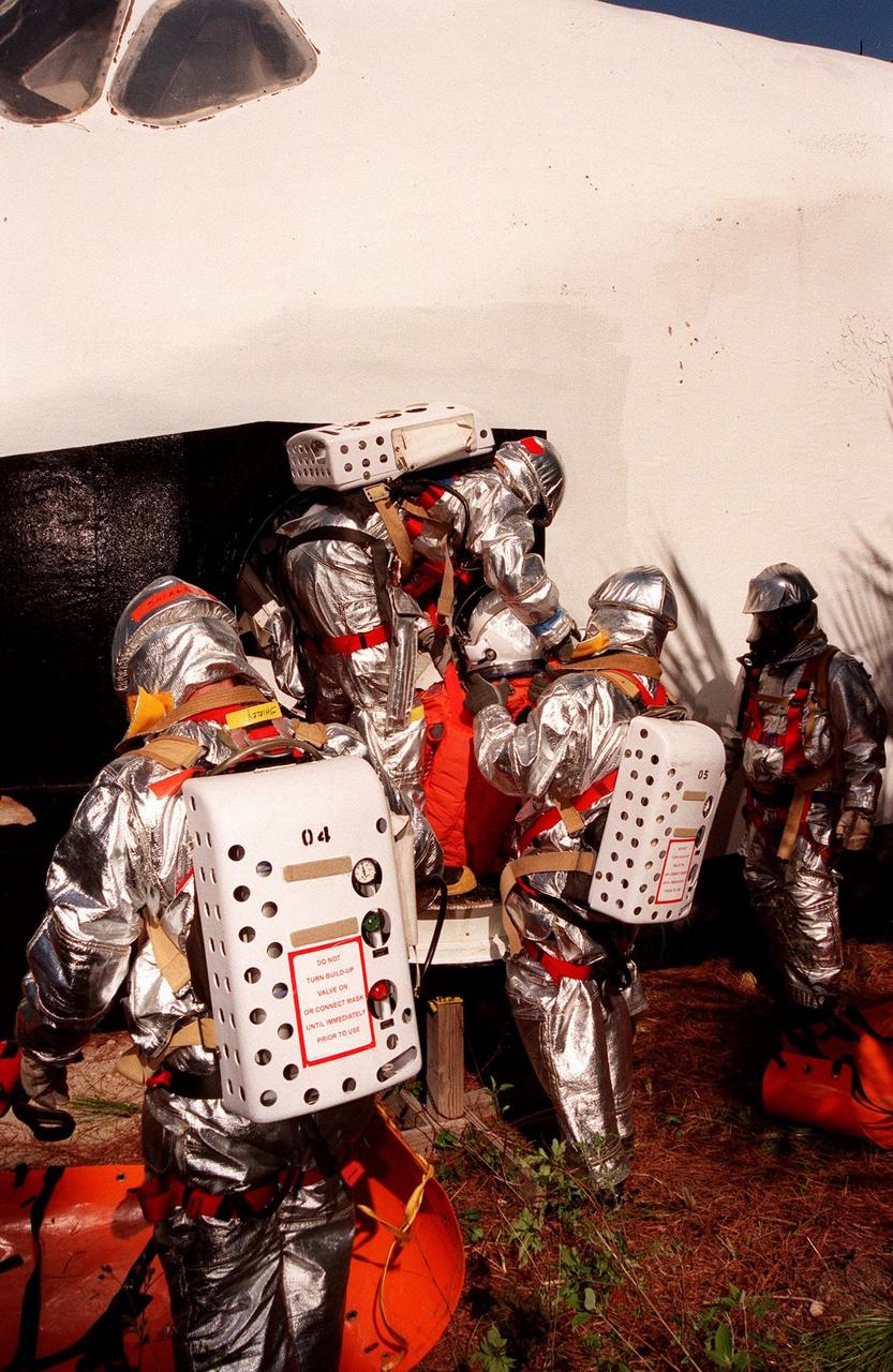 During a simulated rescue mission in the woods near the Shuttle Landing Facility (SLF), the KSC response team removes a crew member from a mock Shuttle. The response team is training for the unlikely scenario of a Shuttle mishap at the SLF. The Mode 7 simulation of an astronaut rescue exercises all aspects of command and control, search and rescue, and medical procedures required for a successful rescue. The remote location of the mock-up prevents a totally land-based crew rescue, and calls on a NASA UH-1 helicopter to locate the site and four Air Force HH-60 helicopters to drop emergency equipment and fire/rescue workers to prepare the "crew" for preliminary triage. The helicopters later are used to remove the crew five astronaut candidates, one representative from the Vehicle Integration Test office, and one fire/rescue worker. The exercise concluded with airlifted "patients" arriving safely in the emergency rooms of participating area hospitals