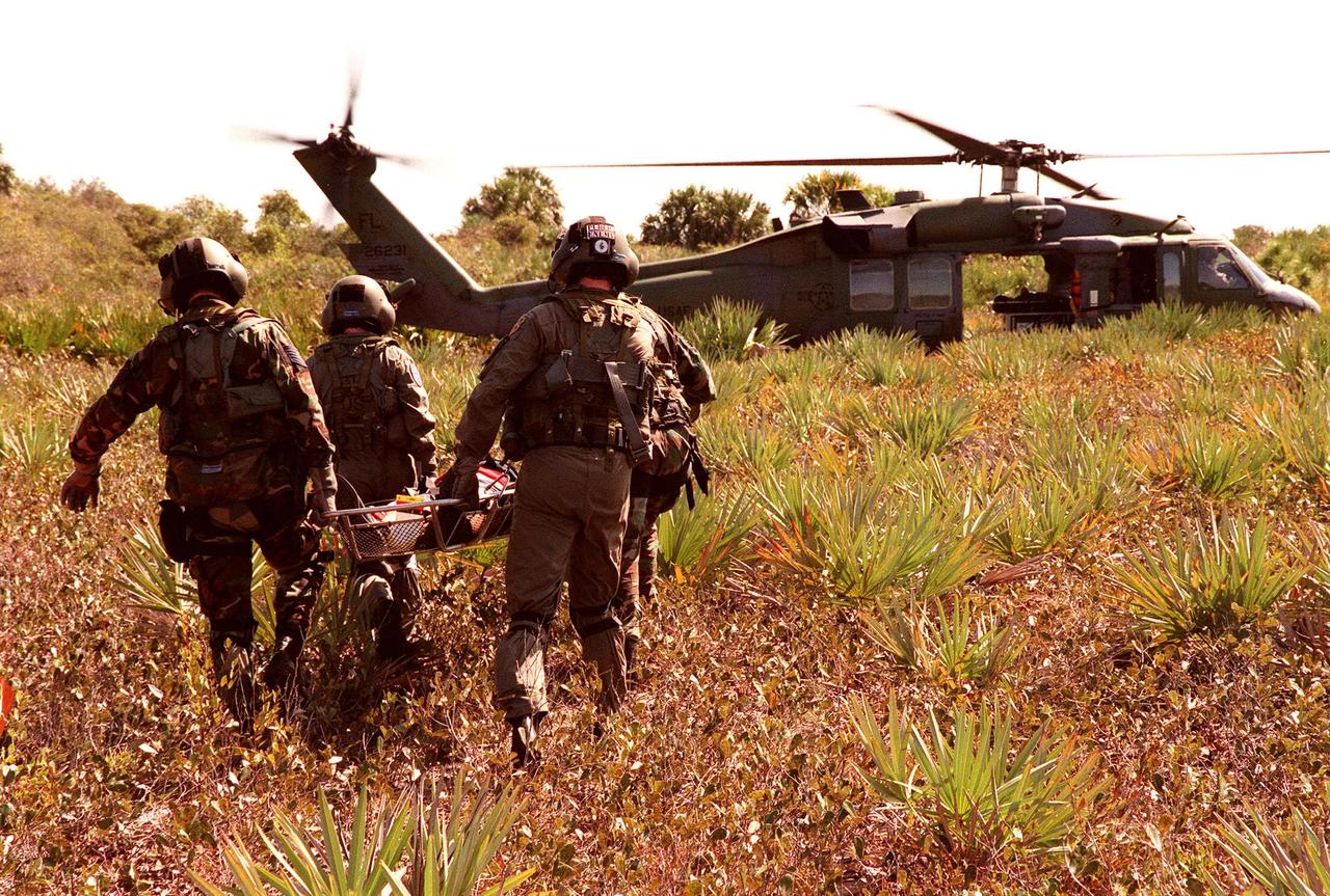 KENNEDY SPACE CENTER, FLA. -- During a simulated rescue mission in the woods near the Shuttle Landing Facility (SLF), the KSC response team practices carrying an injured crew member to an Air Force HH-60 helicopter for transport to a local hospital. The response team is training for the unlikely scenario of a Shuttle mishap at the SLF. The Mode 7 simulation of an astronaut rescue exercises all aspects of command and control, search and rescue, and medical procedures required for a successful rescue. The remote location of the mock-up prevents a totally land-based crew rescue, and calls on a NASA UH-1 helicopter to locate the site and four Air Force HH-60 helicopters to reach the site, drop emergency equipment and later remove the "crew" five astronaut candidates, one representative from the Vehicle Integration Test office, and one fire/rescue worker. The exercise will conclude with airlifted "patients" arriving safely in the emergency rooms of participating area hospitals