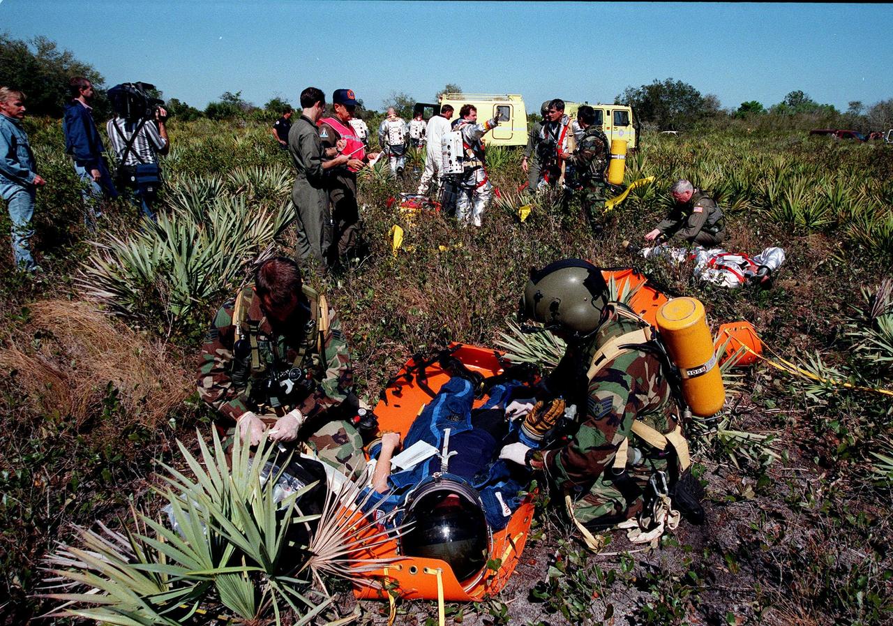 KENNEDY SPACE CENTER, FLA. -- During a simulated rescue mission in the woods near the Shuttle Landing Facility (SLF), the KSC response team practices stabilizing an injured crew member before transport to a local hospital by helicopter. The response team is training for the unlikely scenario of a Shuttle mishap at the SLF. The Mode 7 simulation of an astronaut rescue exercises all aspects of command and control, search and rescue, and medical procedures required for a successful rescue. The remote location of the mock-up prevents a totally land-based crew rescue, and calls on a NASA UH-1 helicopter to locate the site and four Air Force HH-60 helicopters to drop emergency equipment and fire/rescue workers who will prepare the "crew" for preliminary triage. The helicopters later will help remove the crew five astronaut candidates, one representative from the Vehicle Integration Test office, and one fire/rescue worker. The exercise will conclude with airlifted "patients" arriving safely in the emergency rooms of participating area hospitals